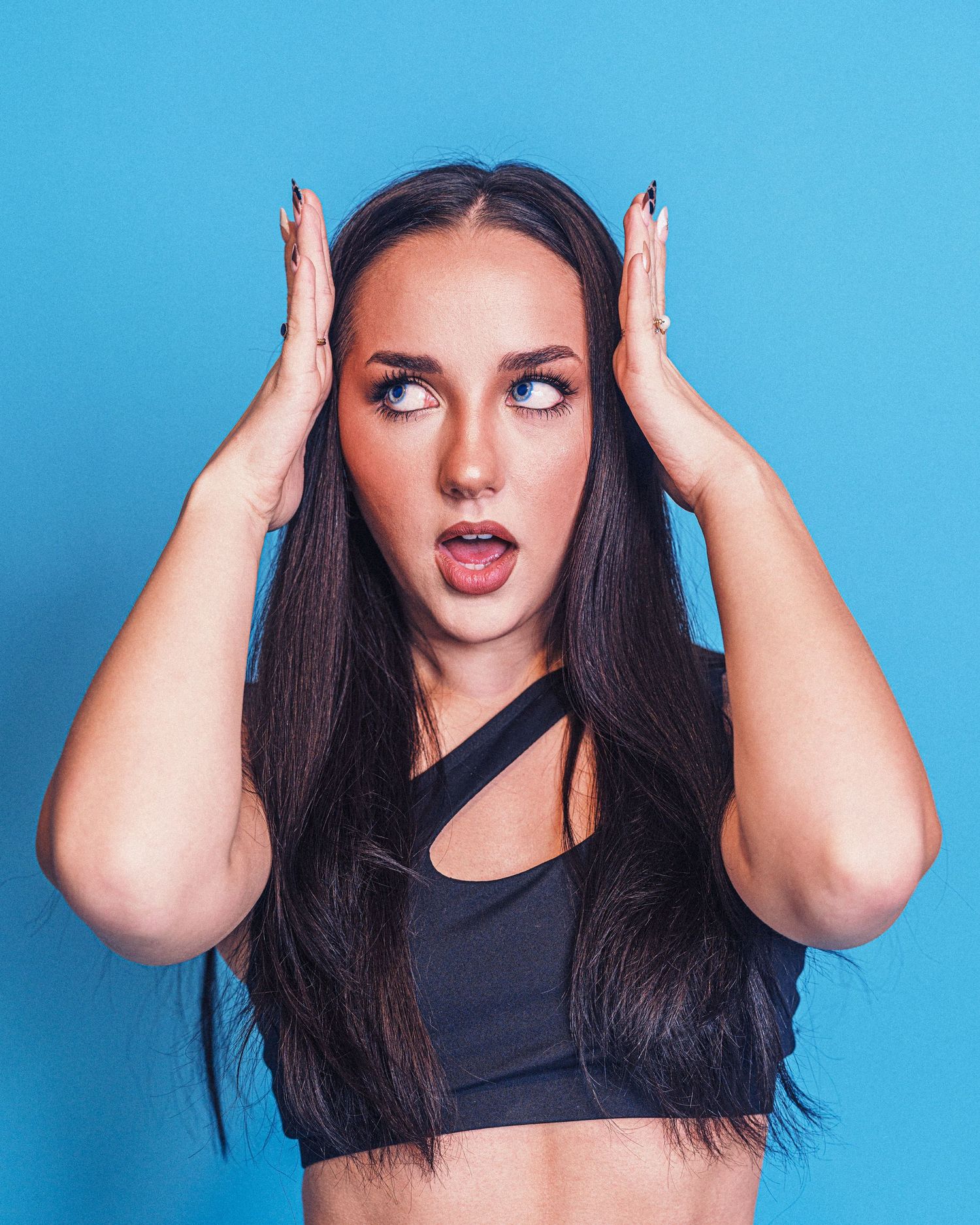 Playful expressions against bright blue background with hands raised to head.