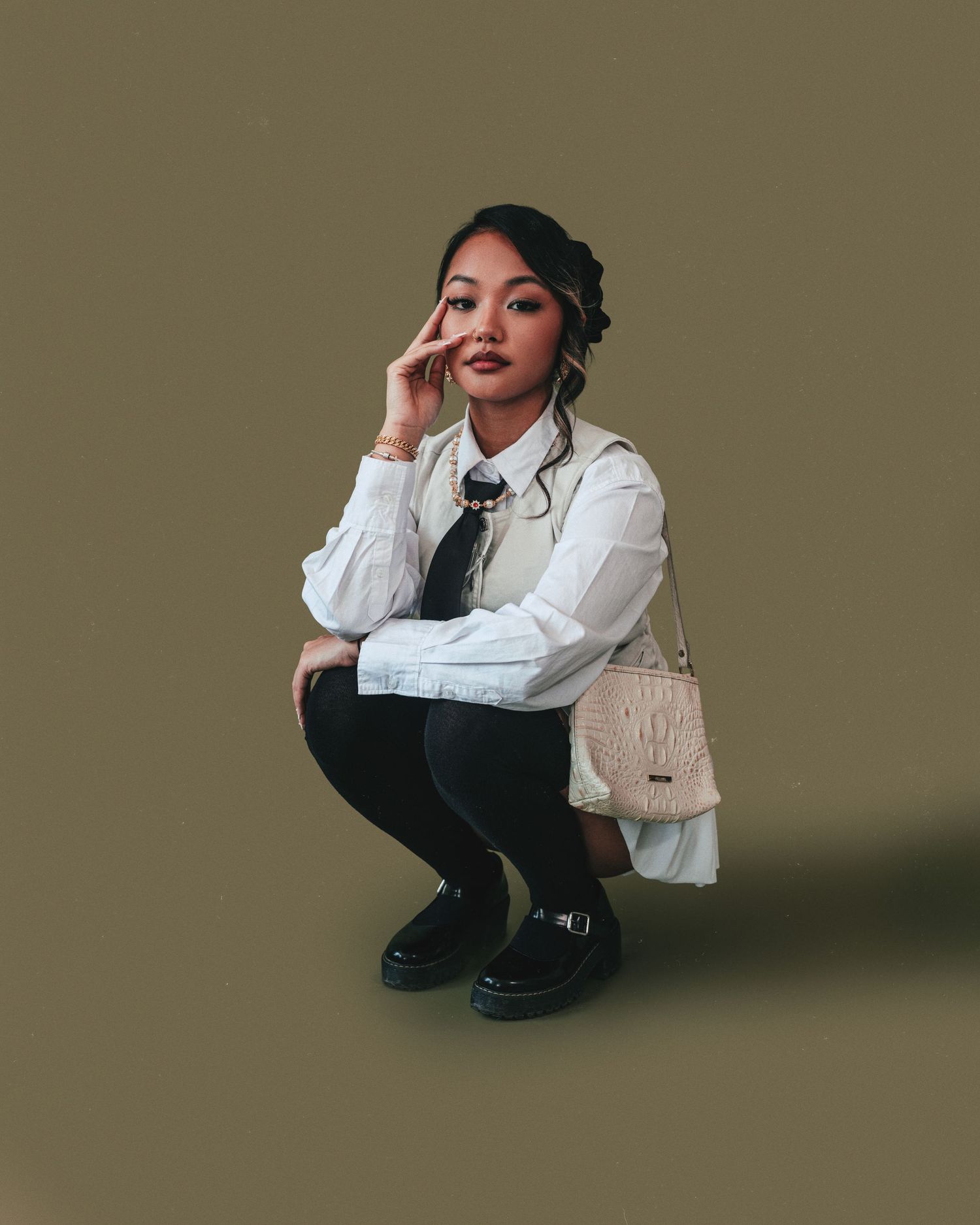 Fashion model in white blazer and black pants poses against olive background with designer handbag.