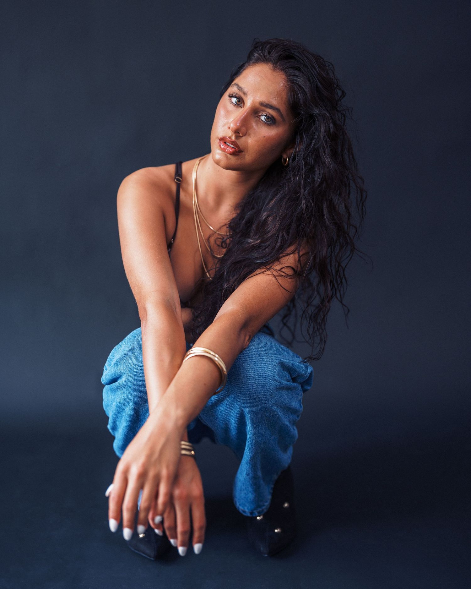 Fashion portrait of model in casual tank top and jeans posing against dark background in studio setting.