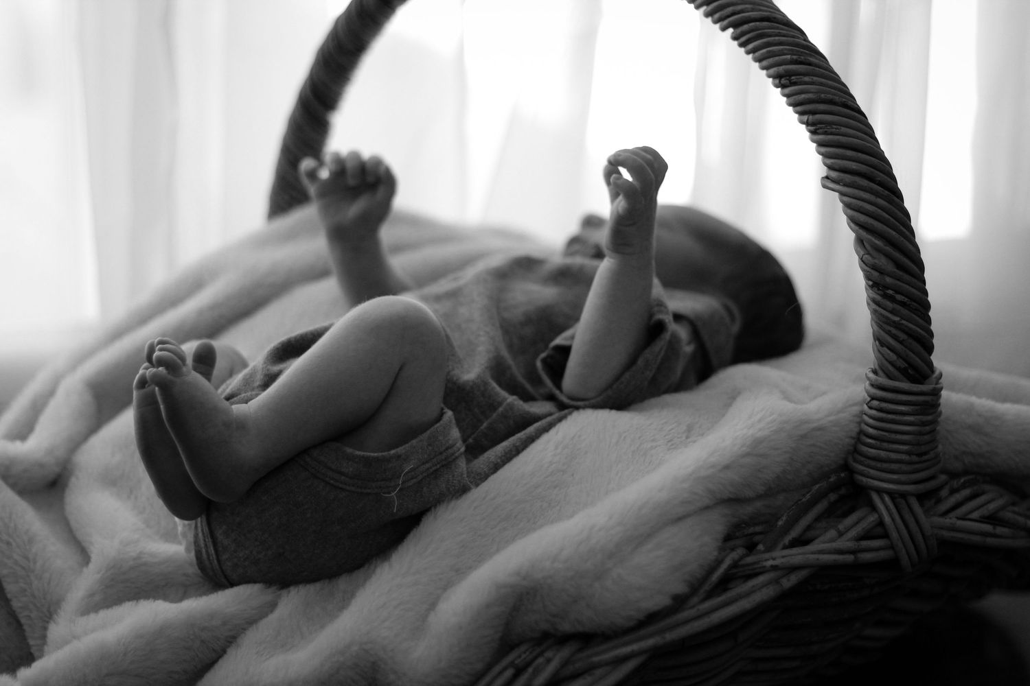 a black & white photo of a newborn baby, laid in a basket, stretching its arms