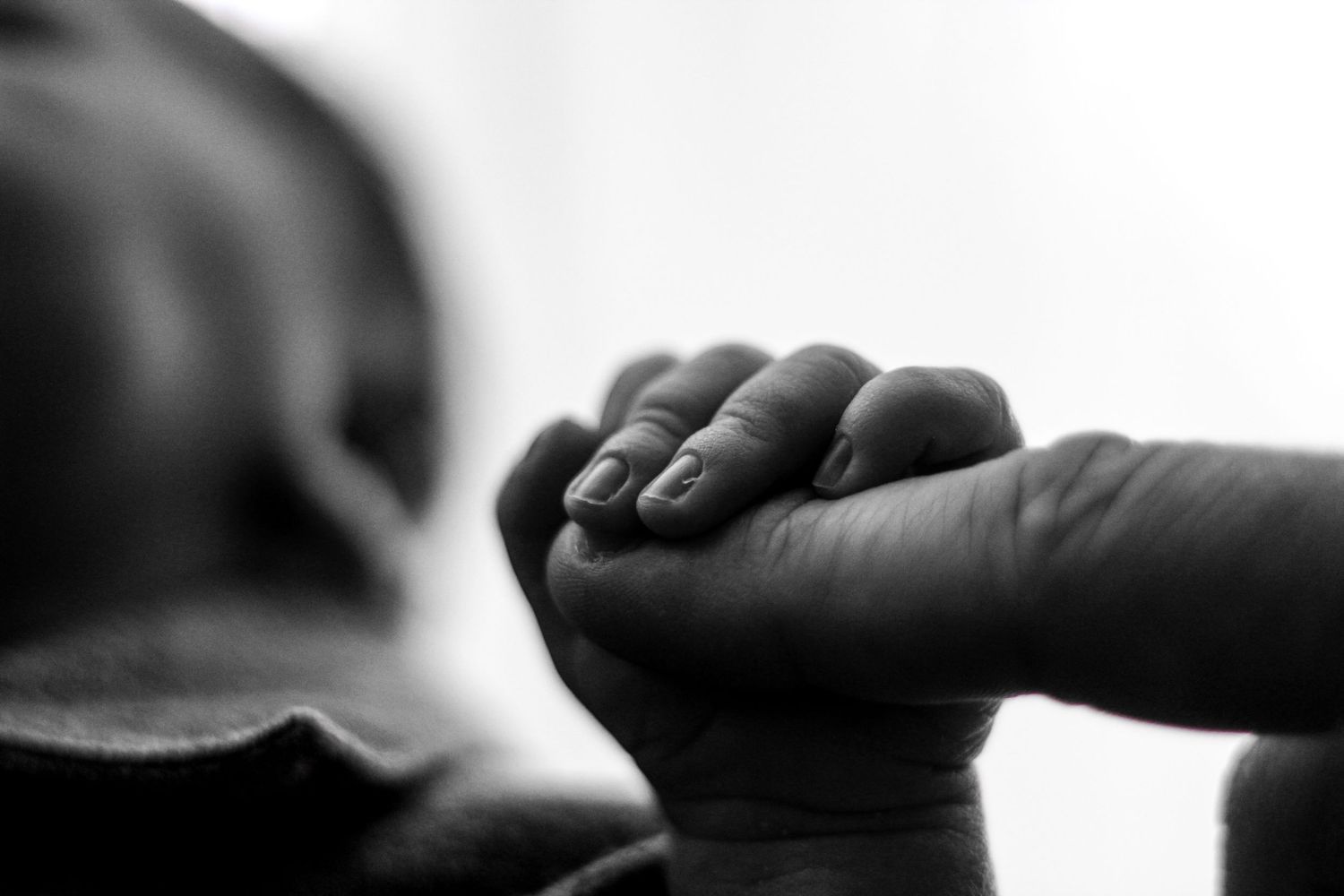 a newborn baby grasping a father's finger. black and white photo