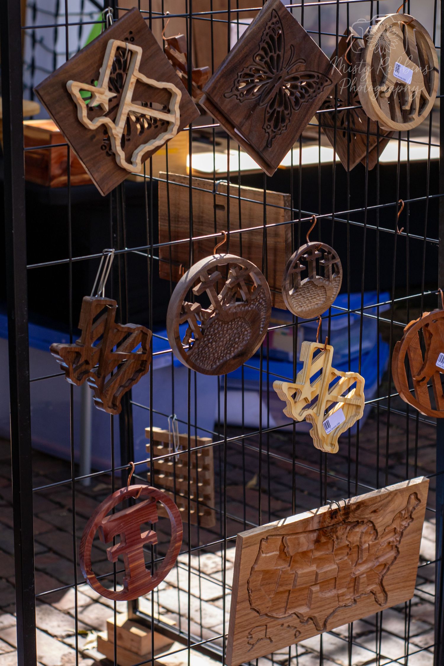 Decorative wooden wall hangings with intricate carved designs displayed on a wire grid.