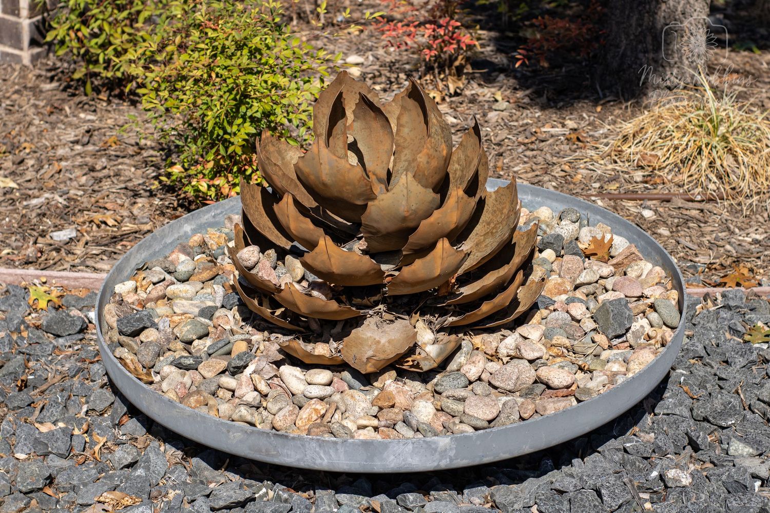 Metal artichoke sculptures arranged on stone beds in a garden display.