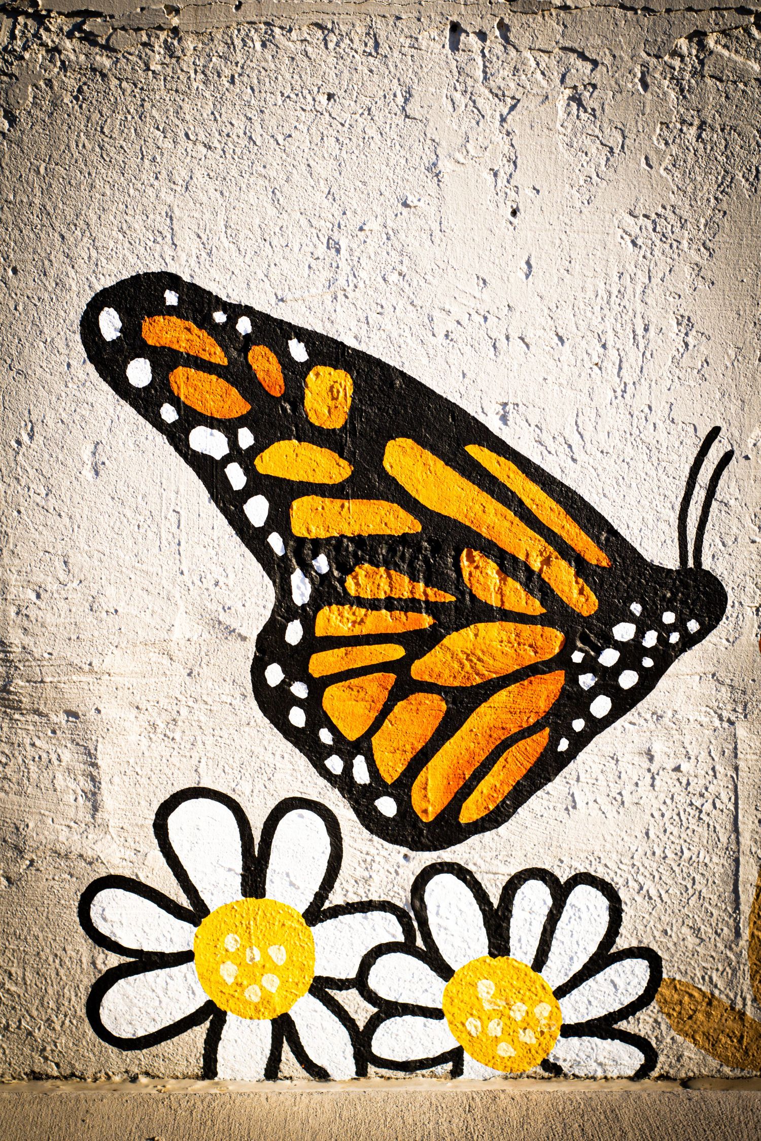 A street art mural showing a monarch butterfly and daisies painted on a textured concrete wall.