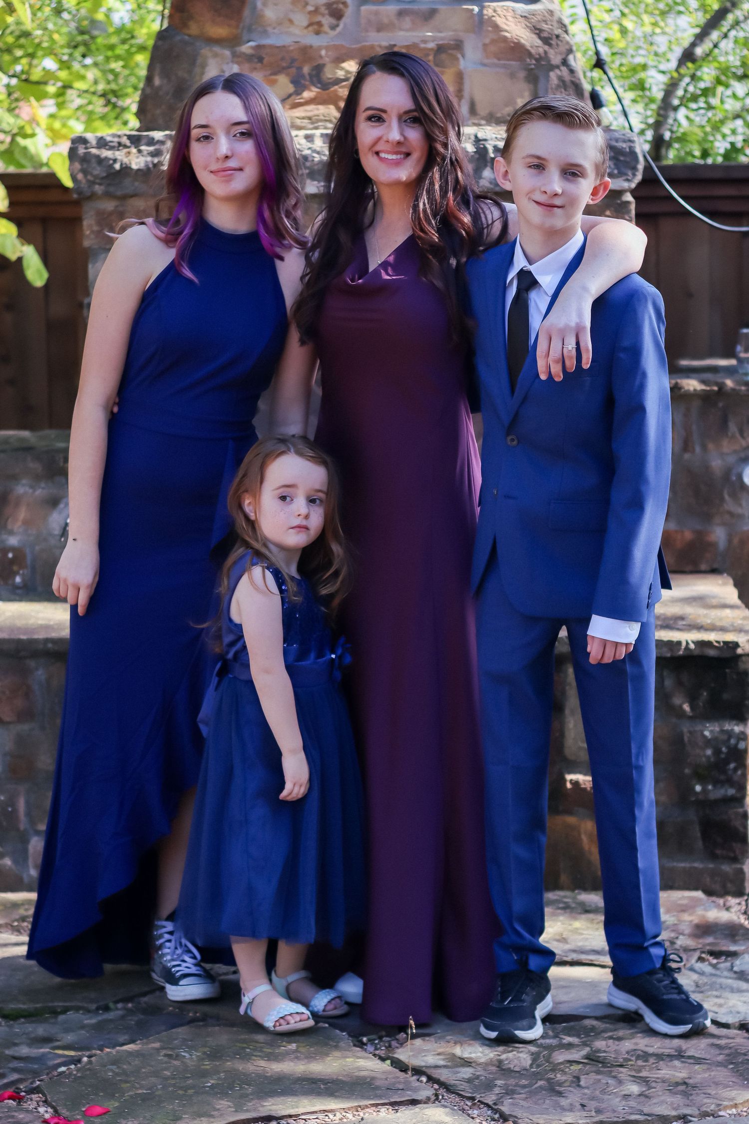 A formal family portrait with four people wearing coordinating navy blue and burgundy formal attire.