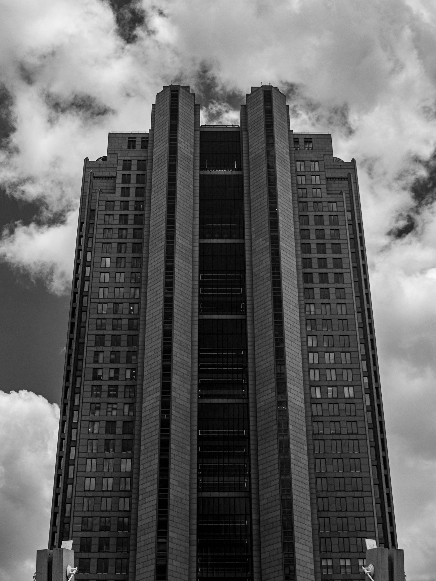 Black and white photo of a tall modern skyscraper shot from below against a cloudy sky.