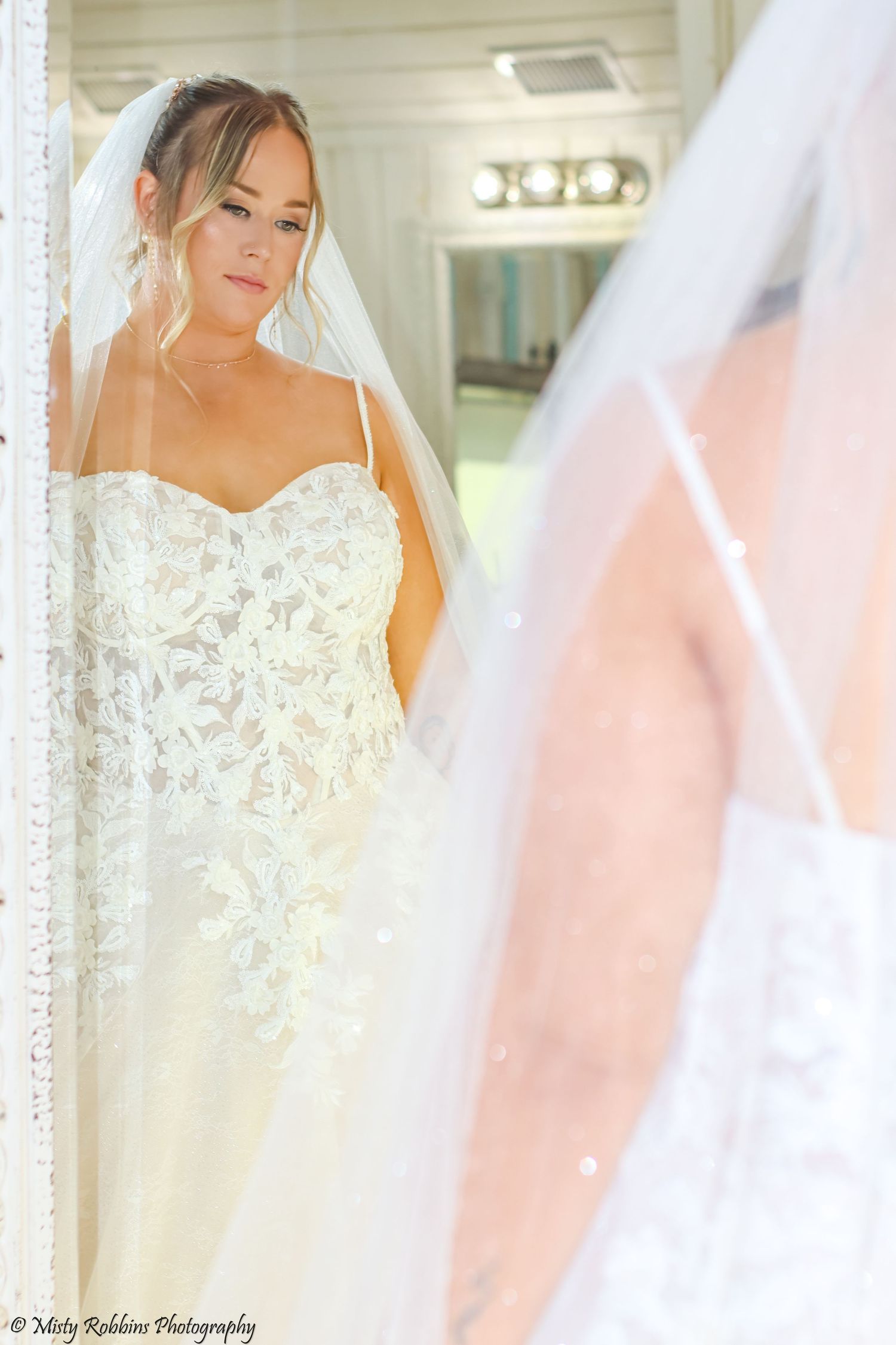 Beautiful bride in white lace wedding dress poses with veil in elegant bridal portraits.