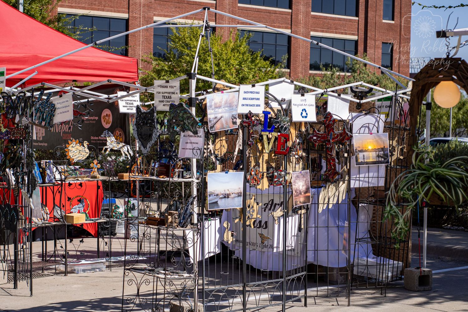 Street view of market stalls with red tents and hanging banners along an urban sidewalk.