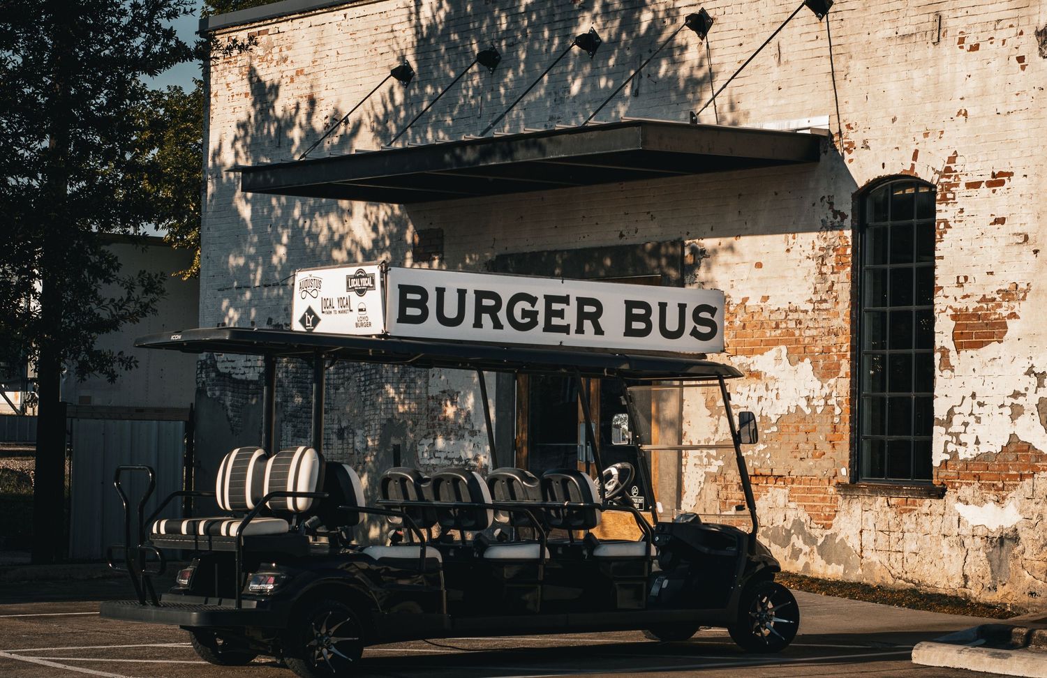Vintage-style Burger Bus food stand with brick wall backdrop in warm afternoon light.