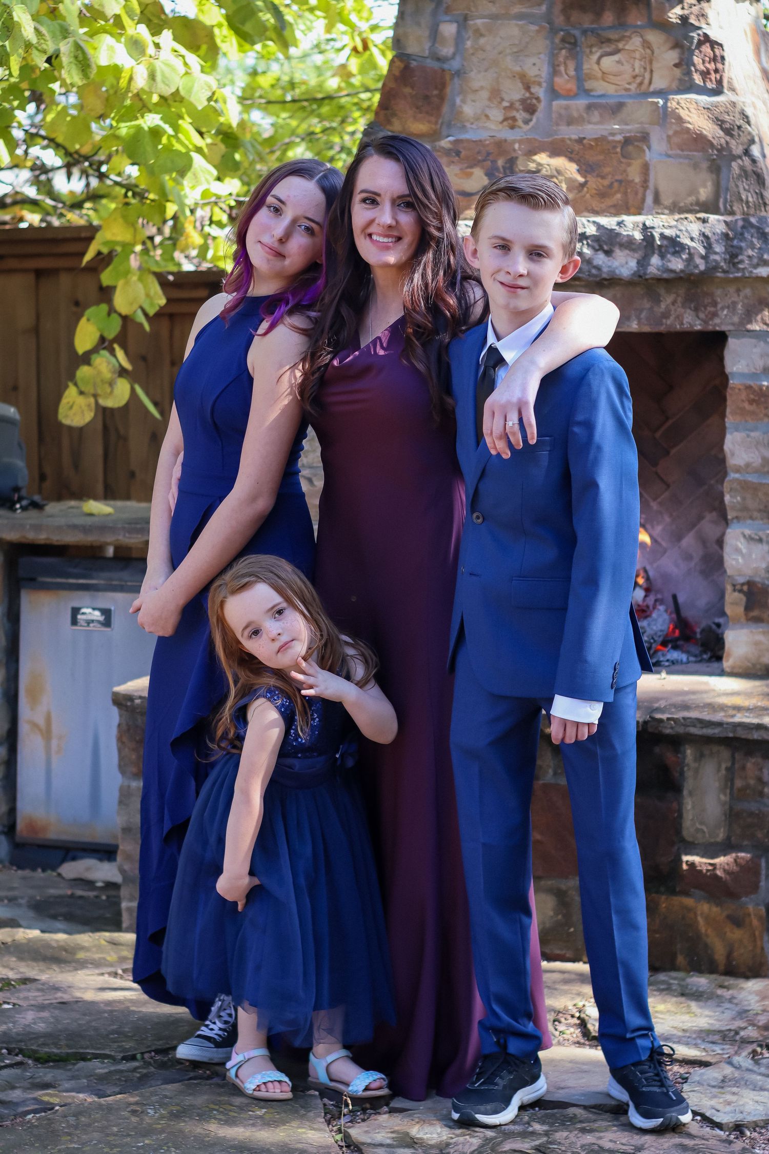 A group poses in coordinating formal wear of navy blue and burgundy against a stone fireplace backdrop.
