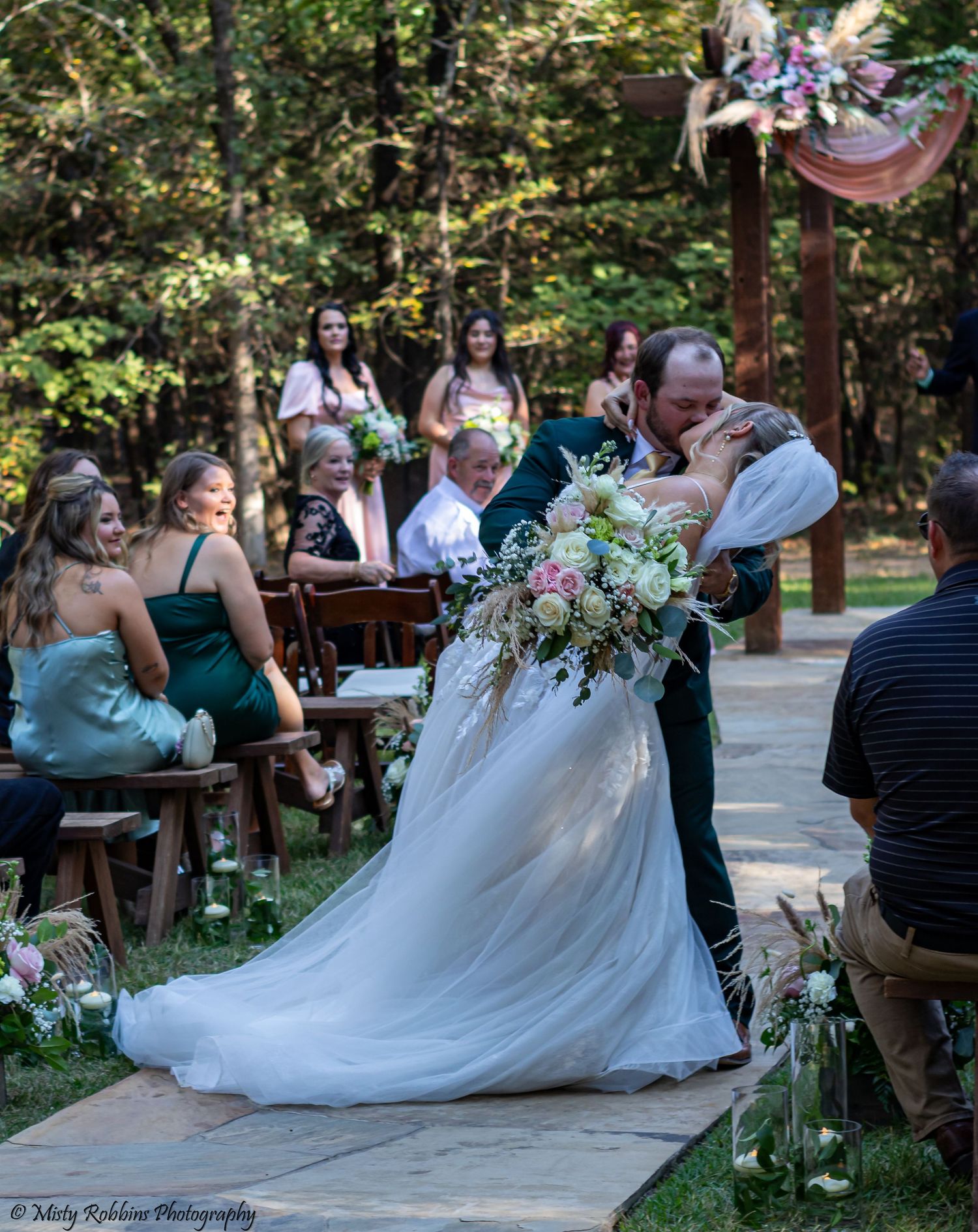 Wedding guests enjoy a lively dance party on an outdoor patio surrounded by trees and string lights.