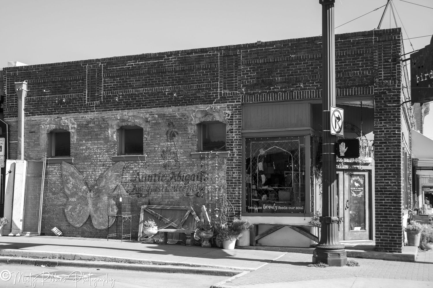 Black and white photo of a brick corner building with butterfly mural and small shops in a downtown area.