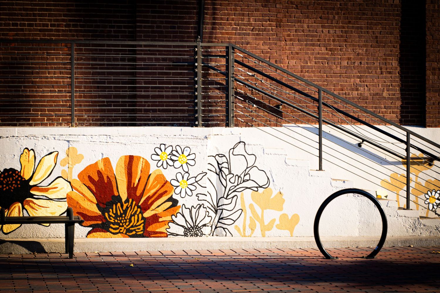 Decorative floral mural with orange flowers painted on white wall beside metal staircase and railing.