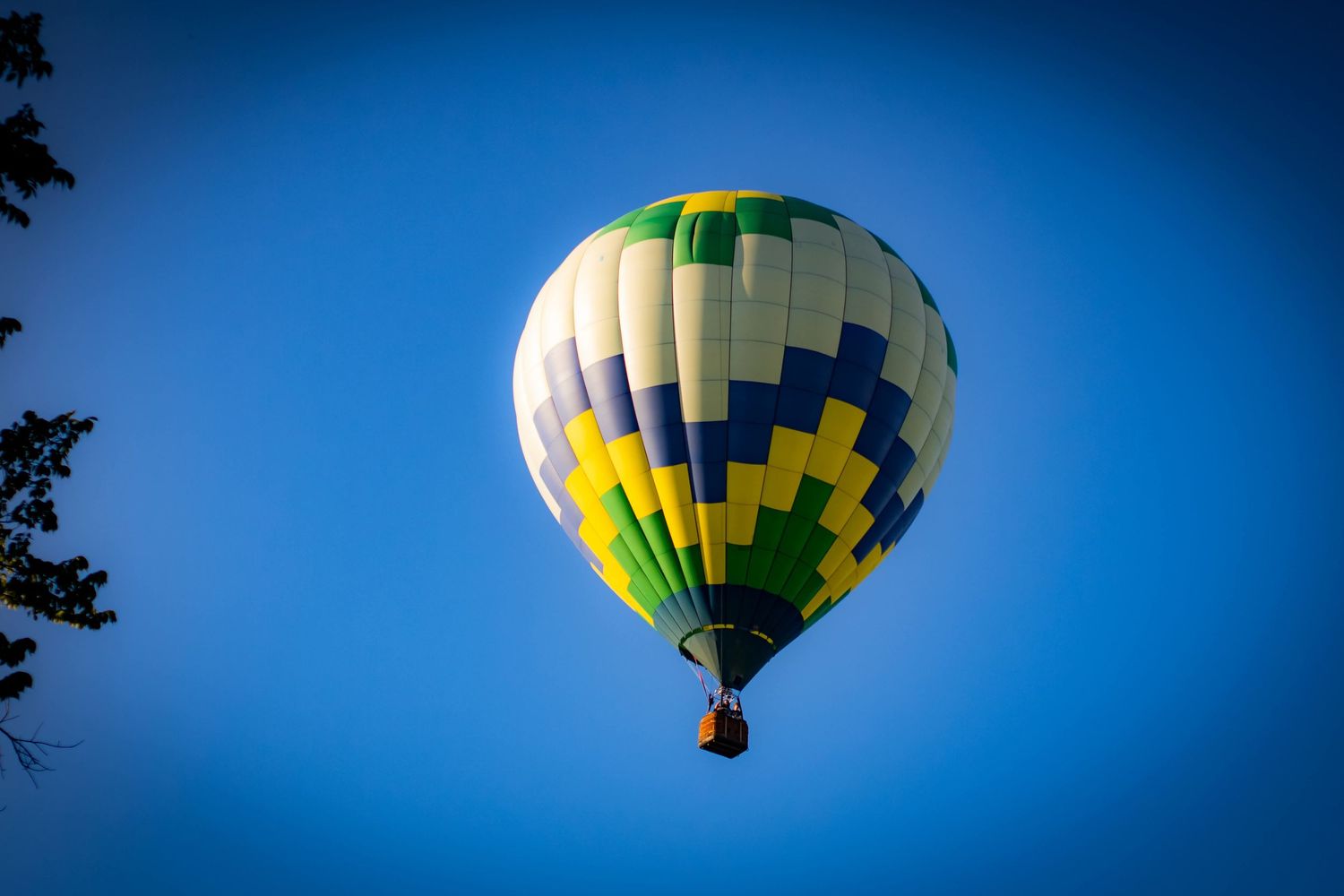 A colorful hot air balloon with yellow and green geometric patterns floats against a deep blue sky.
