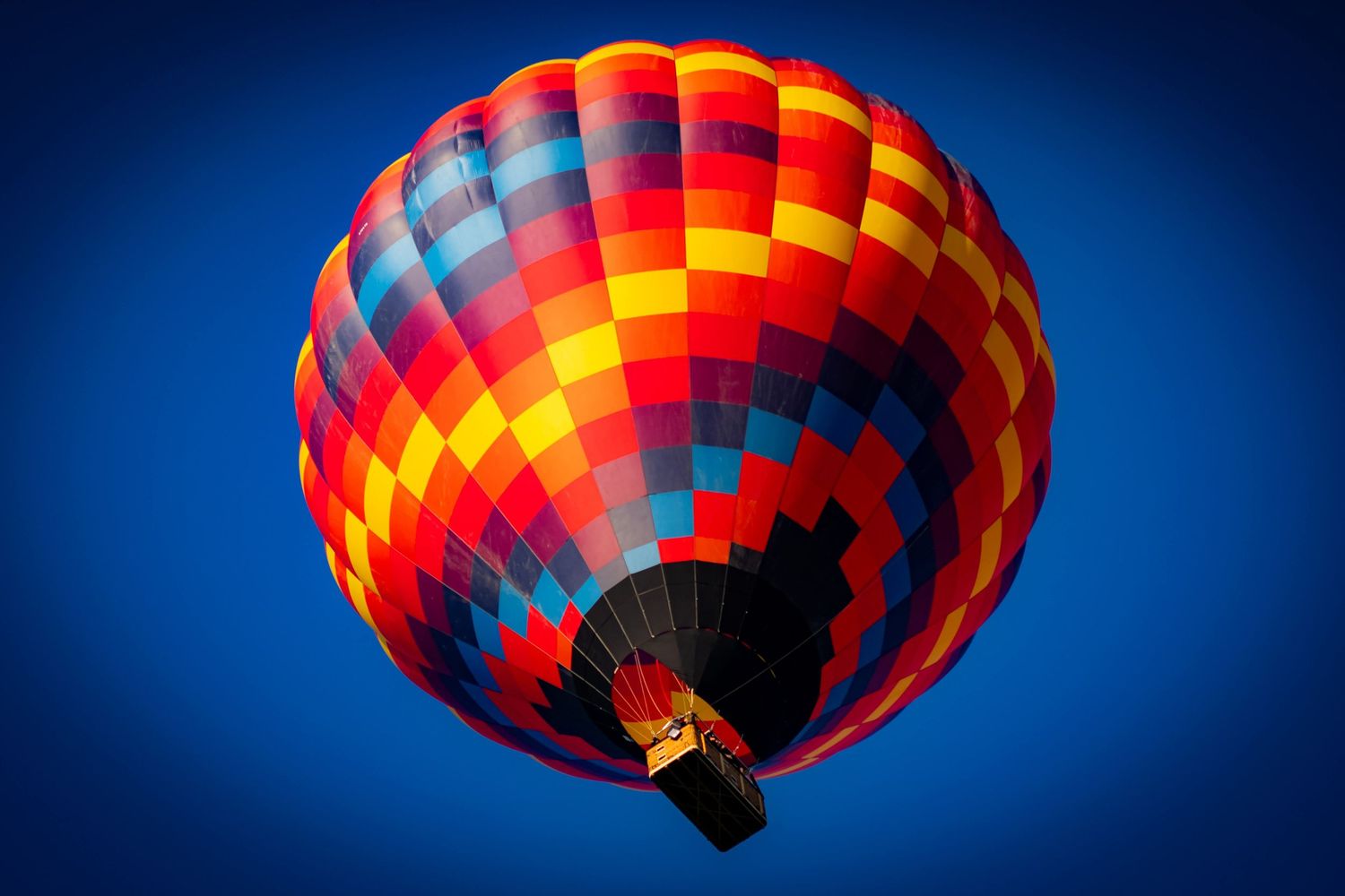 A bright red and yellow hot air balloon silhouetted against a deep blue sky in progressive stages of deflation.