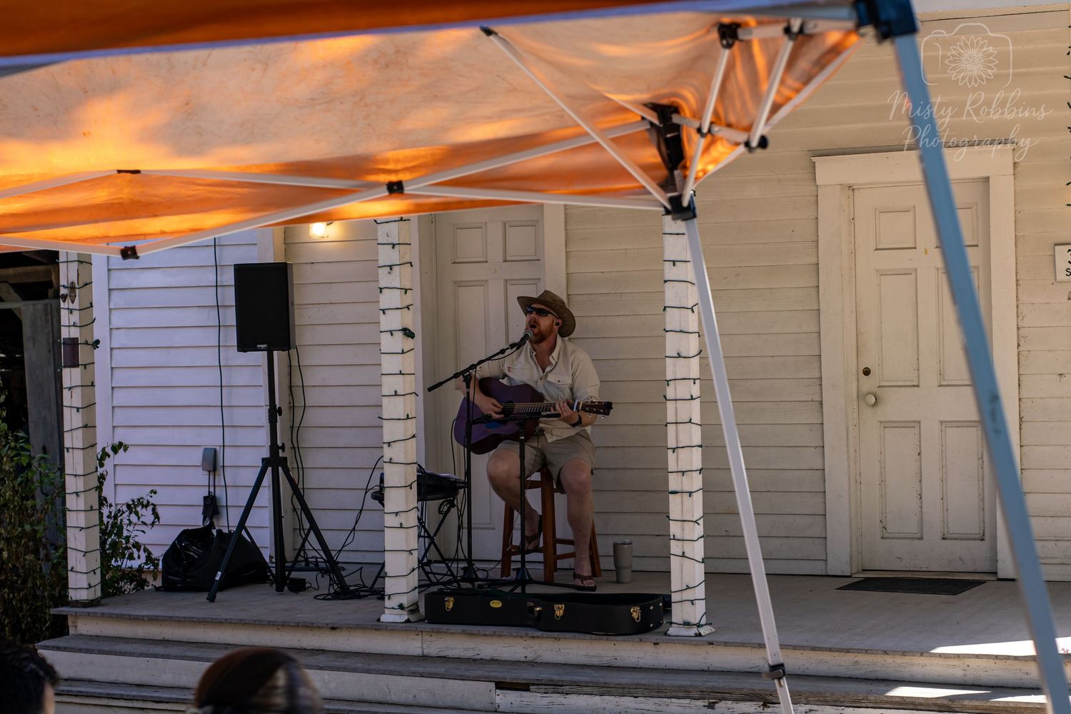 Outdoor setup with canopy tents and equipment being arranged in a backyard or patio space during sunset.