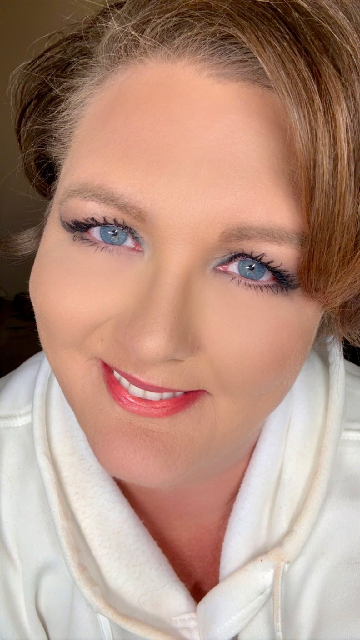 A person wearing a white robe shows off bright blue eyeshadow and pink lipstick in a series of selfie photos.