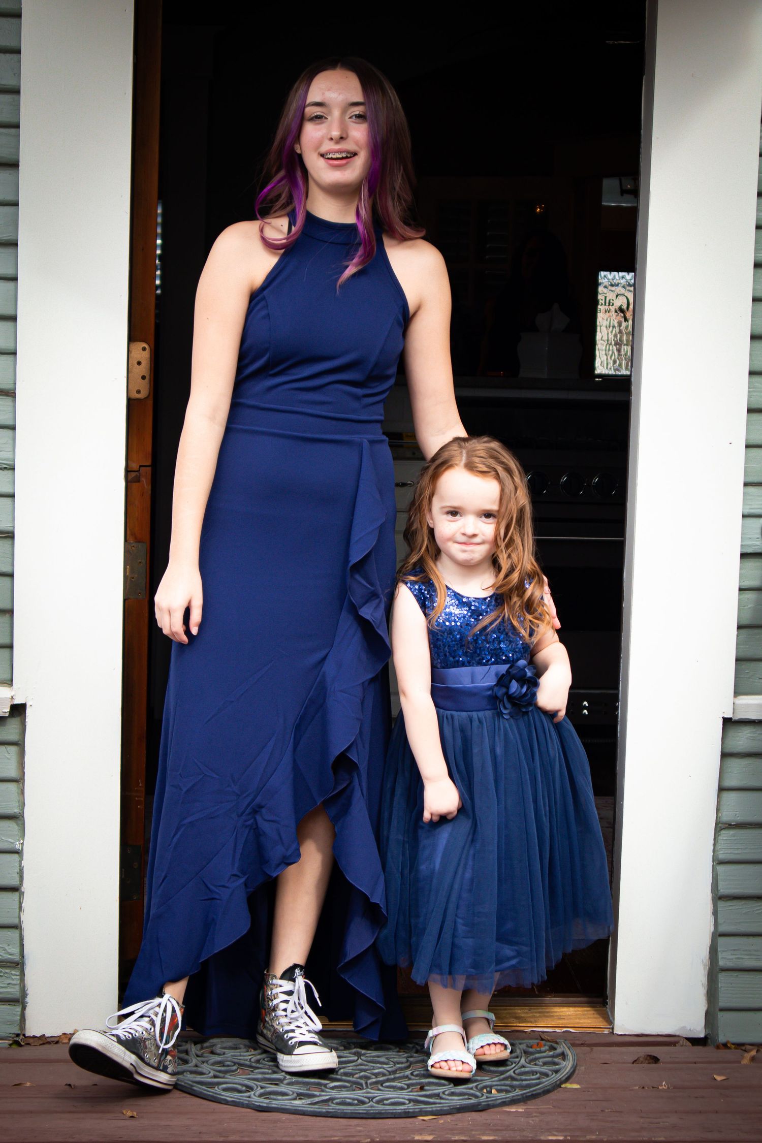 Mother and daughter wearing matching navy blue dresses pose together on a porch.