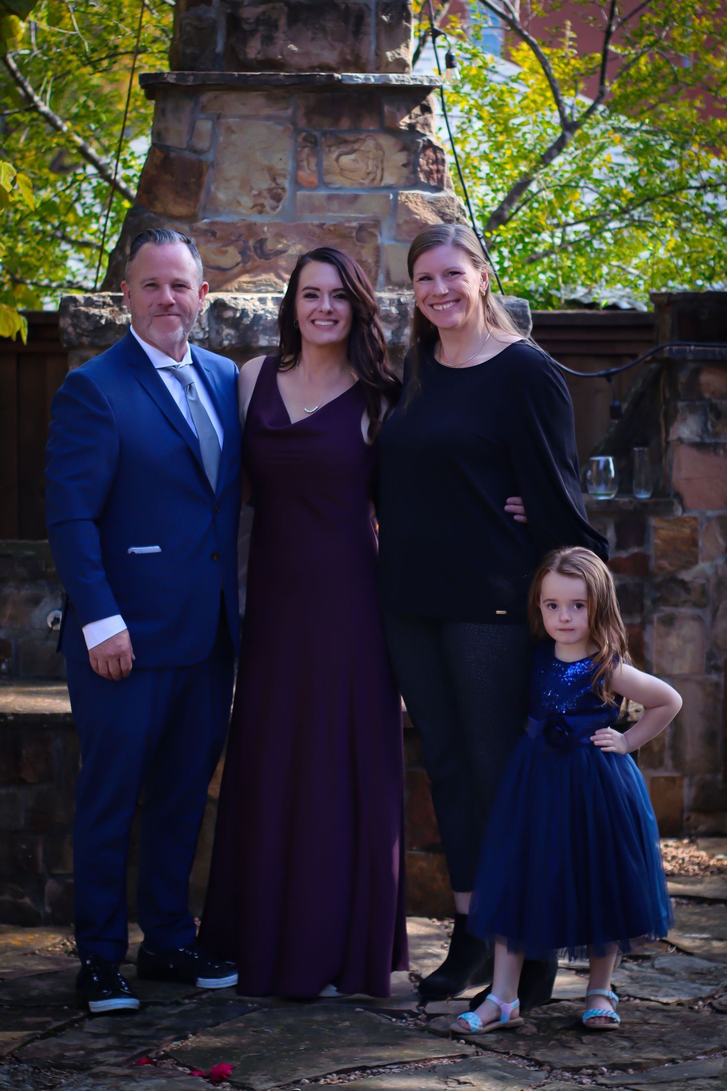 Family gathering on stone patio with brick pillars wearing formal attire in navy and burgundy colors.