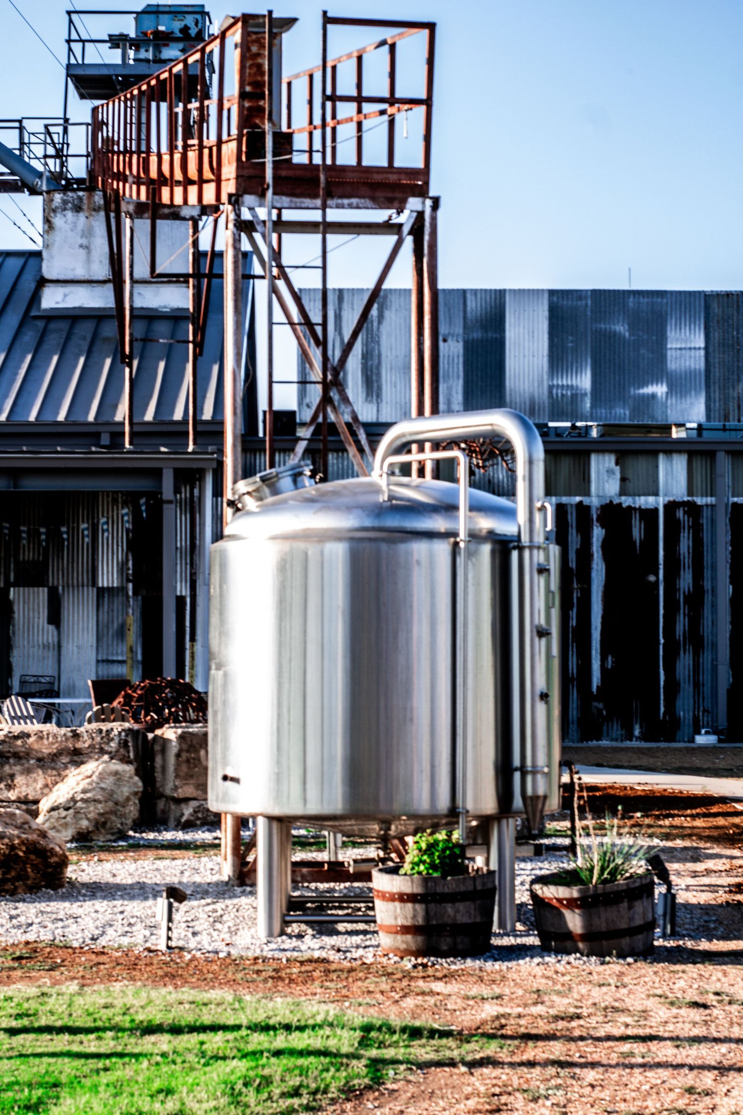 Industrial storage tanks and equipment in an outdoor facility with green grass and gravel ground.
