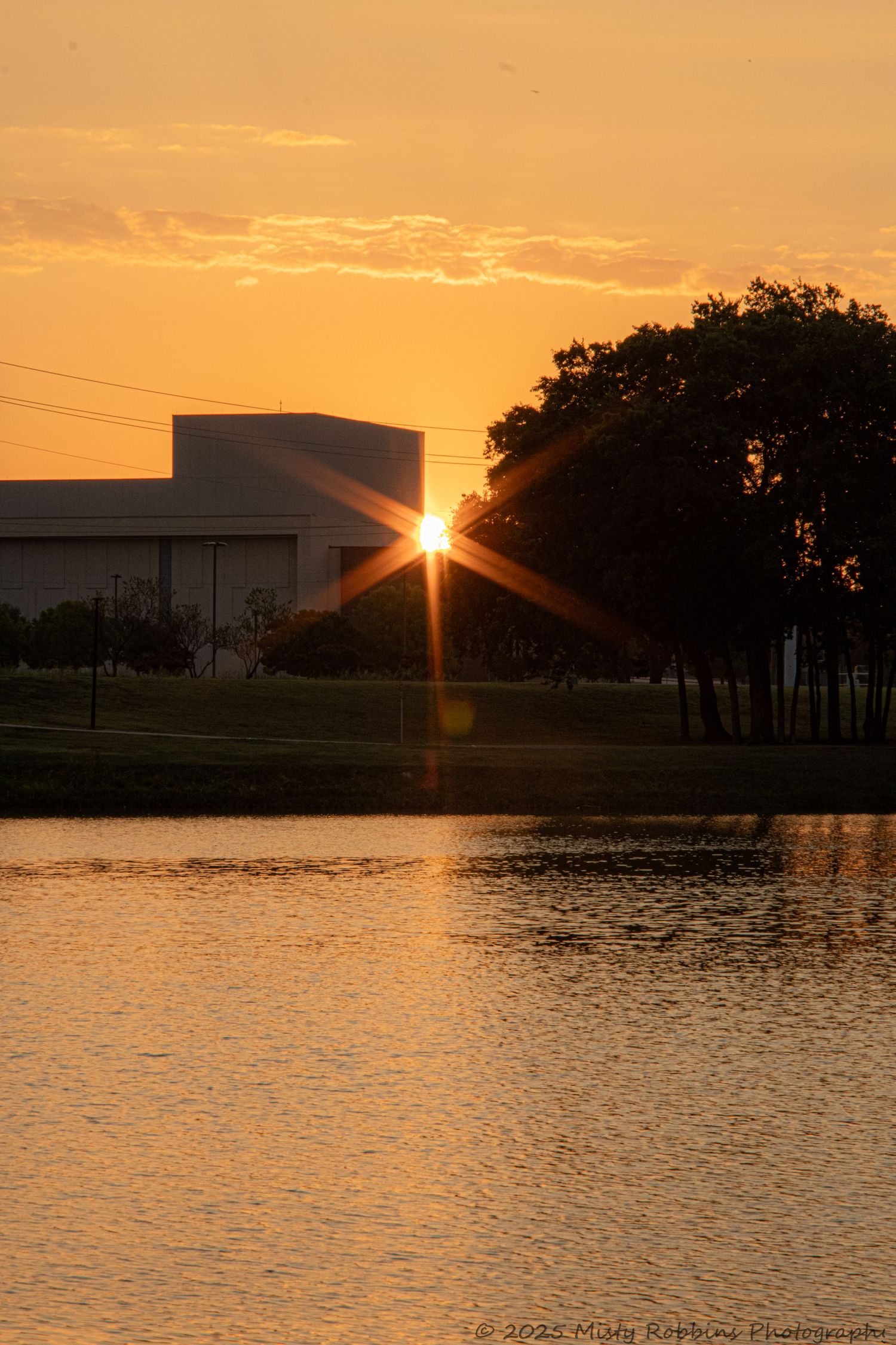 Dramatic orange sunset over a lake with buildings silhouetted against the glowing sky.