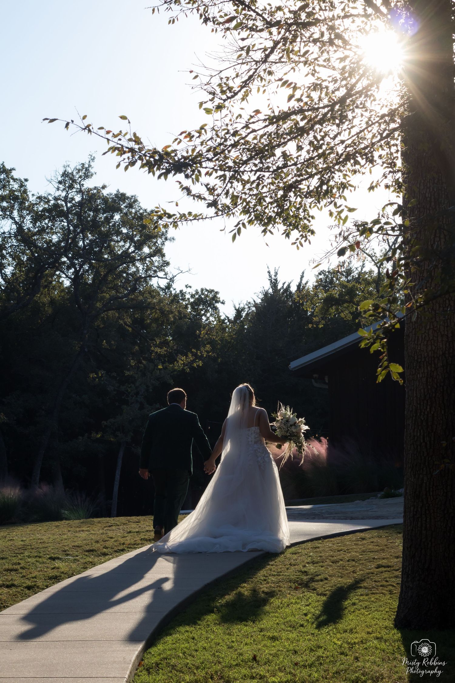Silhouette of a couple walking along a sunlit path during golden hour with trees casting long shadows.