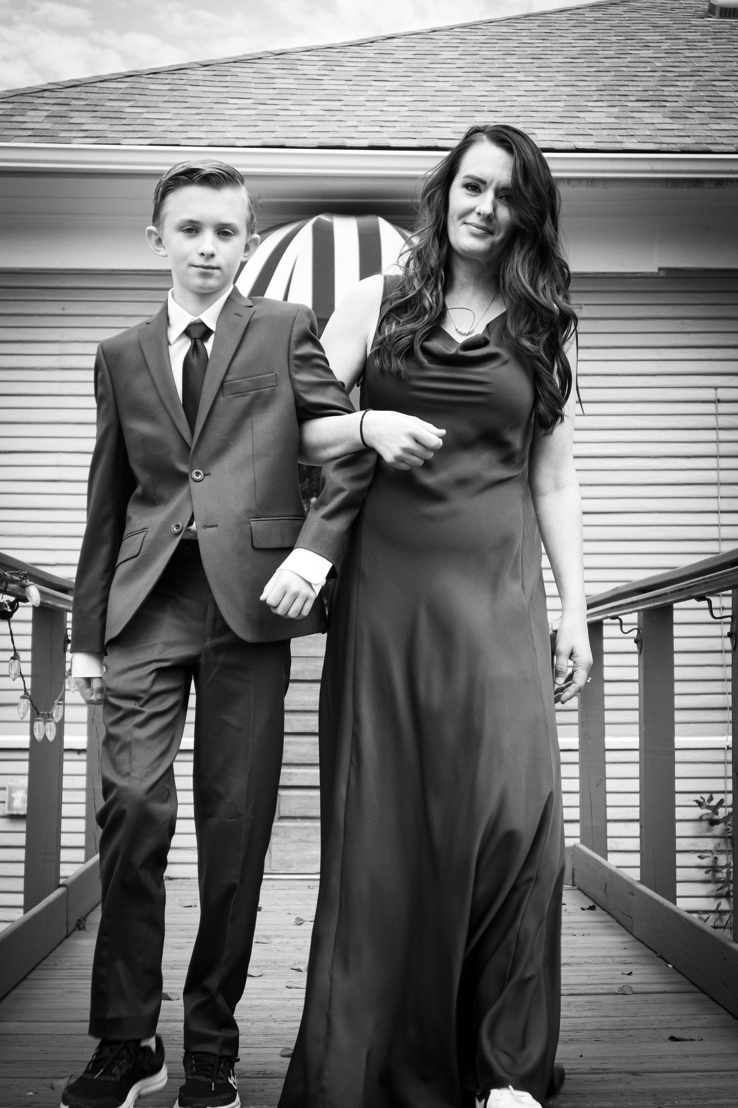 A formal portrait of two people in elegant attire standing on a wooden deck.