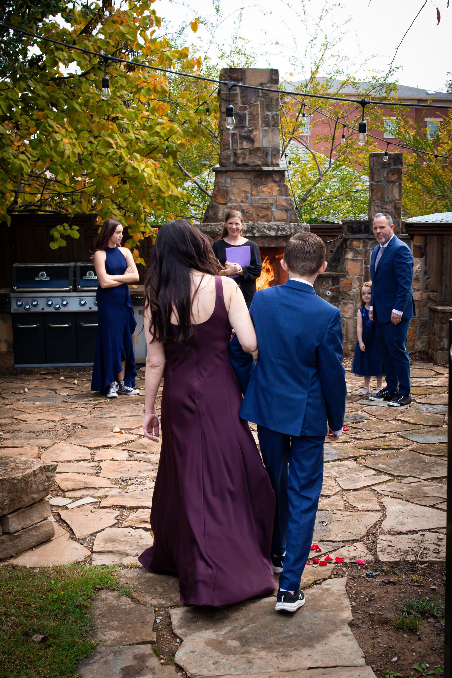 Wedding party poses on rustic stone patio with autumn foliage in background wearing purple and navy formal attire.