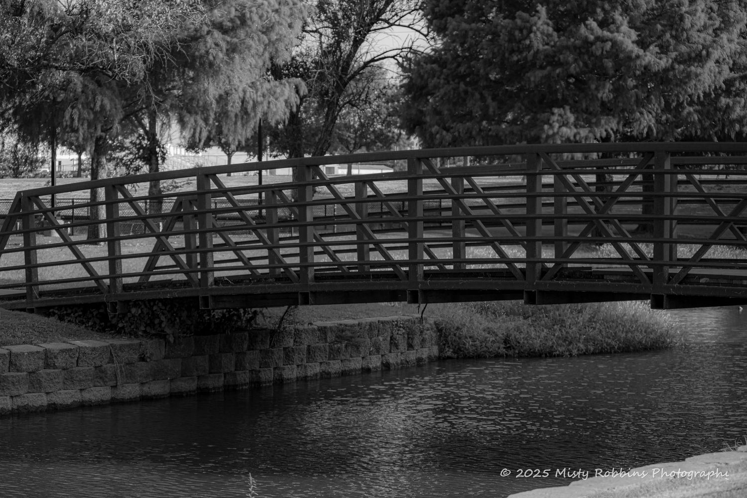A panoramic view of a wooden bridge over a river with trees and fencing along the sides.