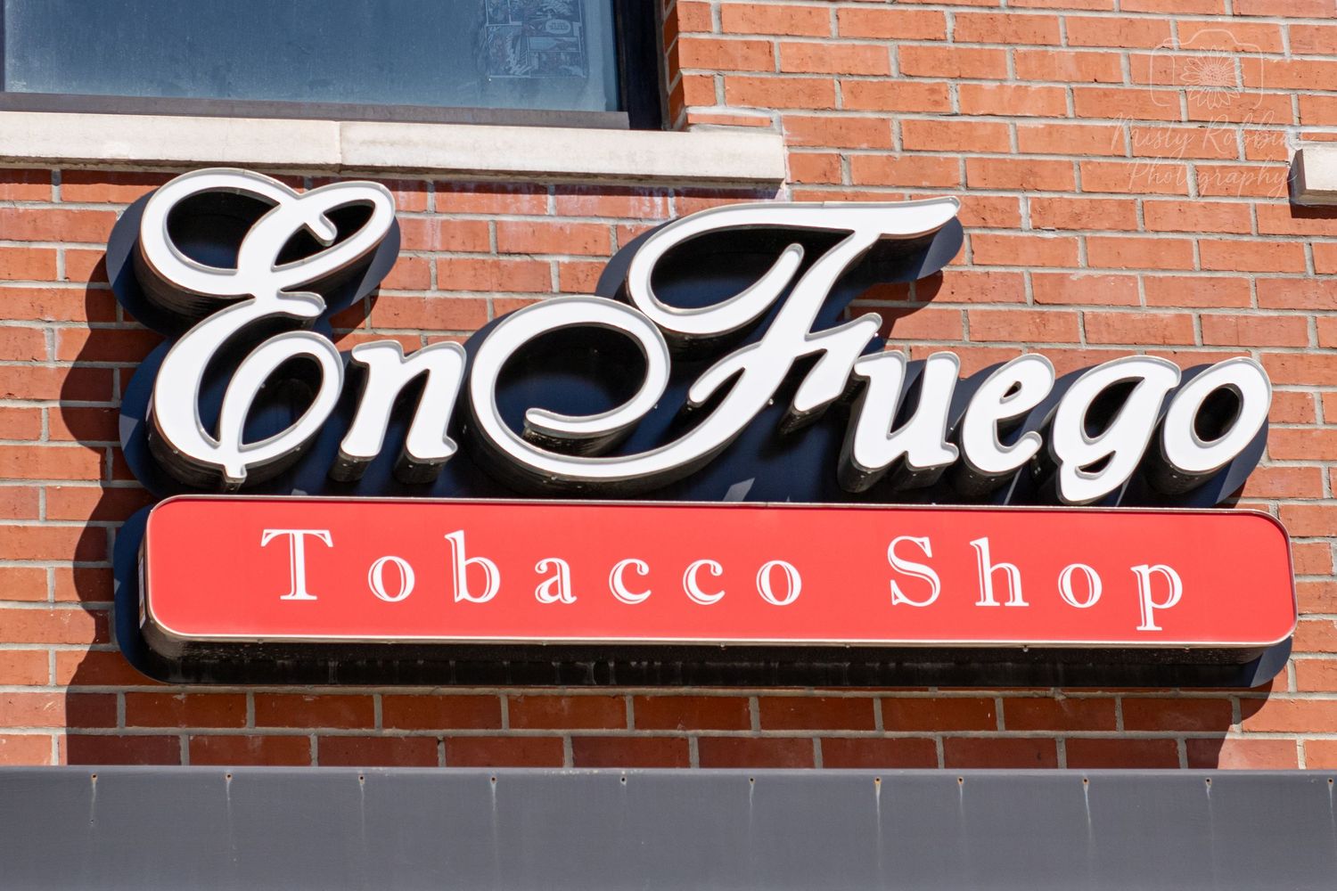 A storefront sign reading 'En Fuego Tobacco Shop' mounted on a red brick wall.