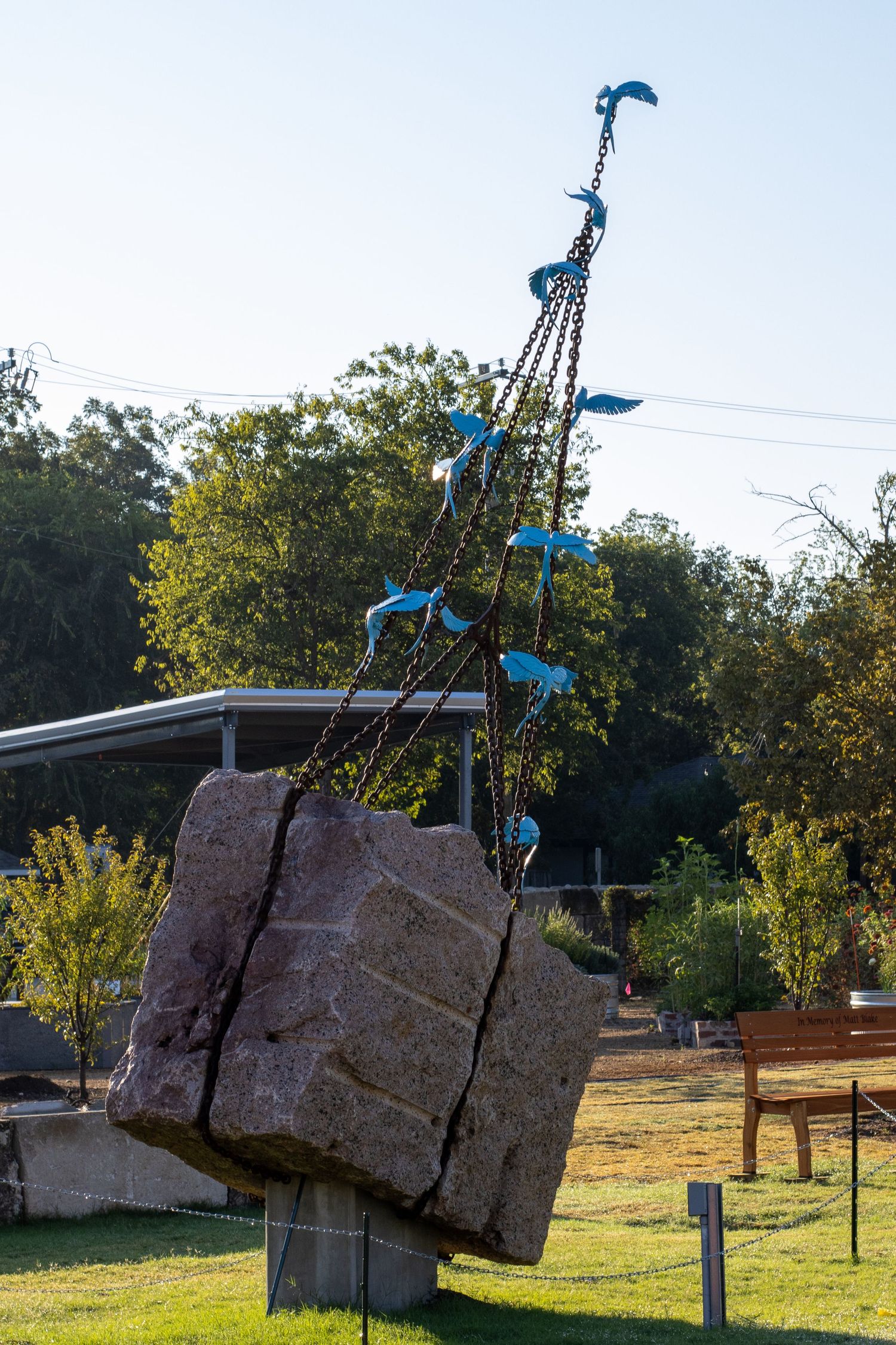 Large sculptural rocks suspended from metal poles with blue flags in an outdoor installation.