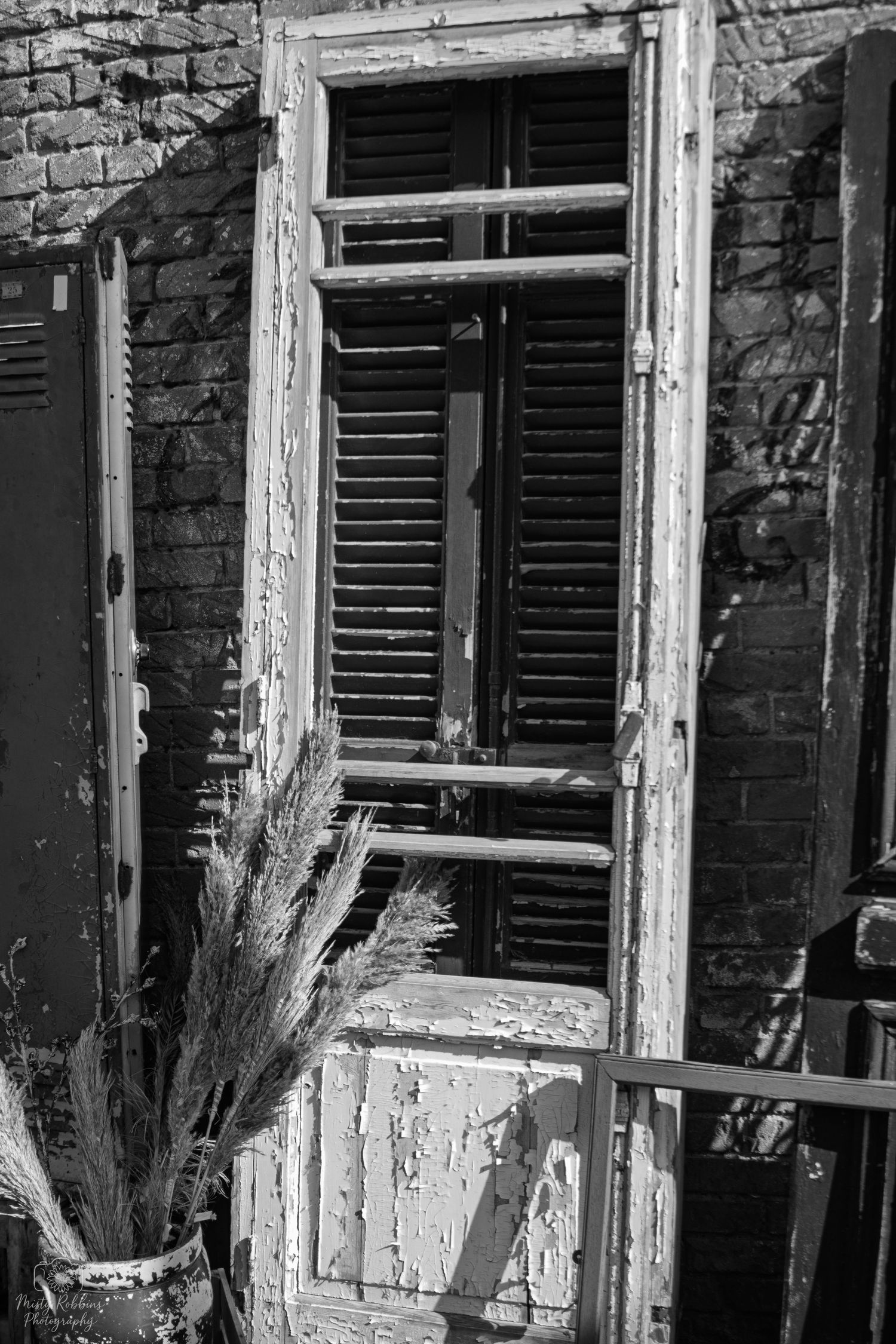 Black and white architectural detail of weathered brick building with peeling paint and shuttered windows.