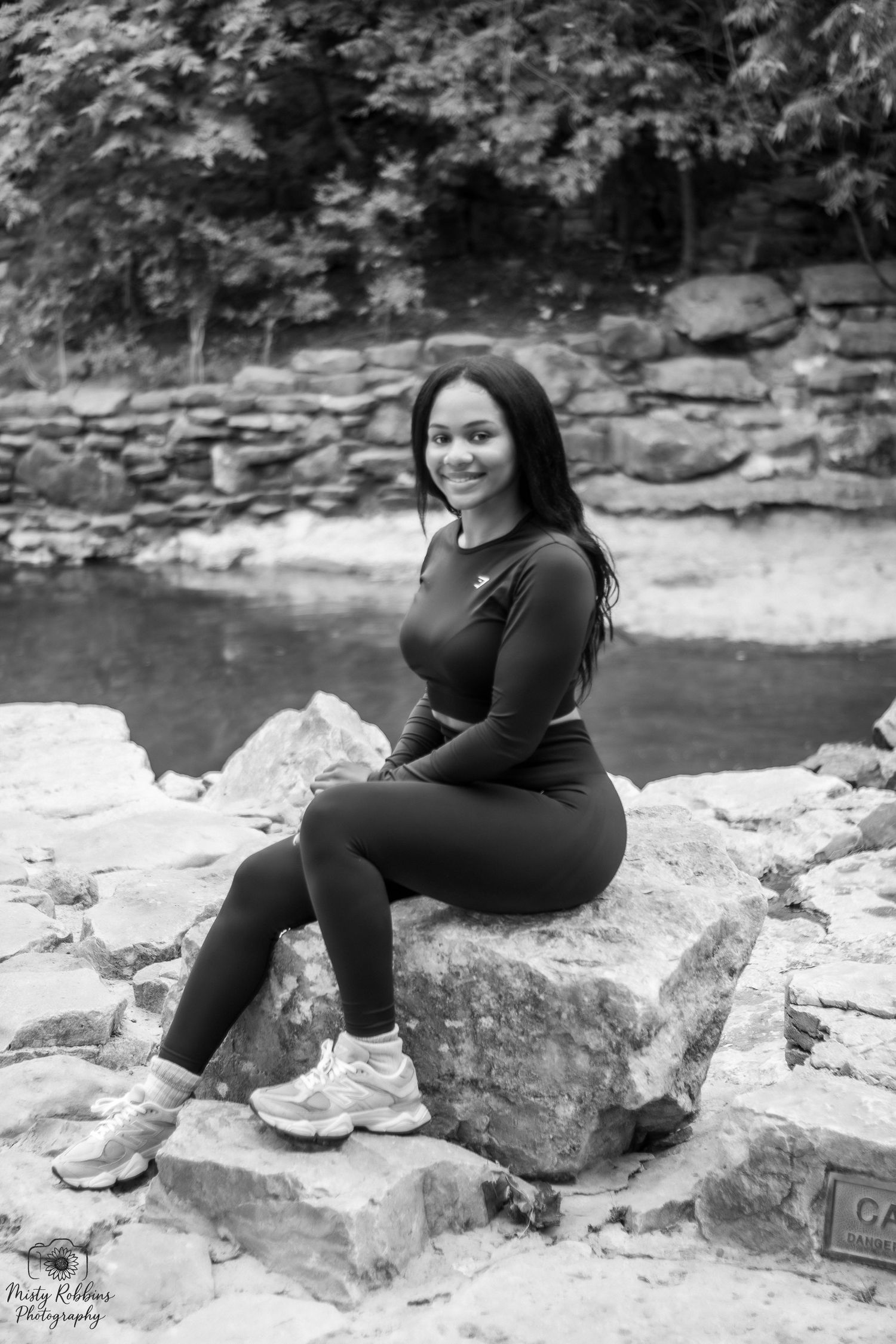 A figure in all black sits on rocky terrain by a riverbank in a series of black and white portraits.
