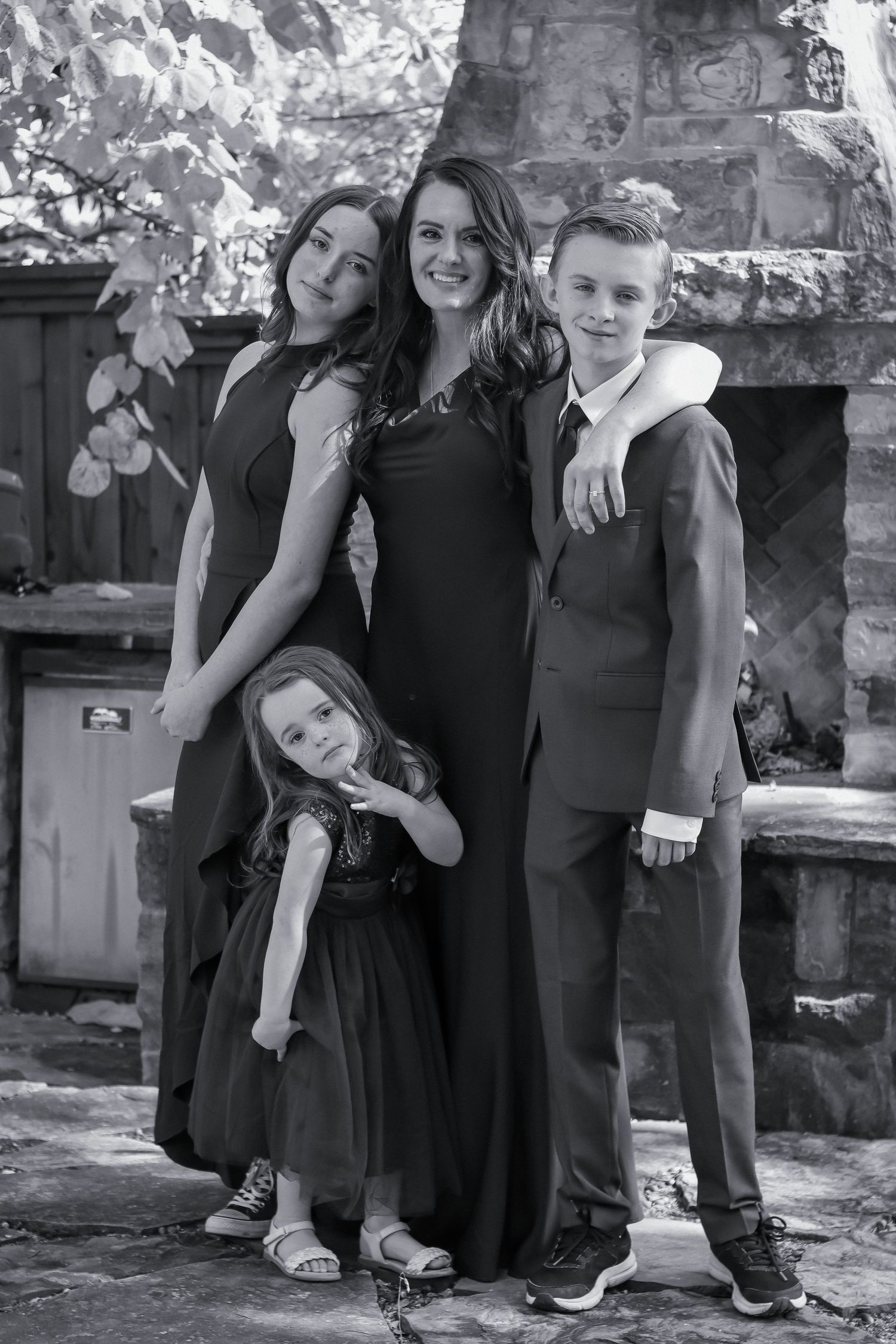 A black and white portrait of a group posing together by a stone fireplace outdoors.