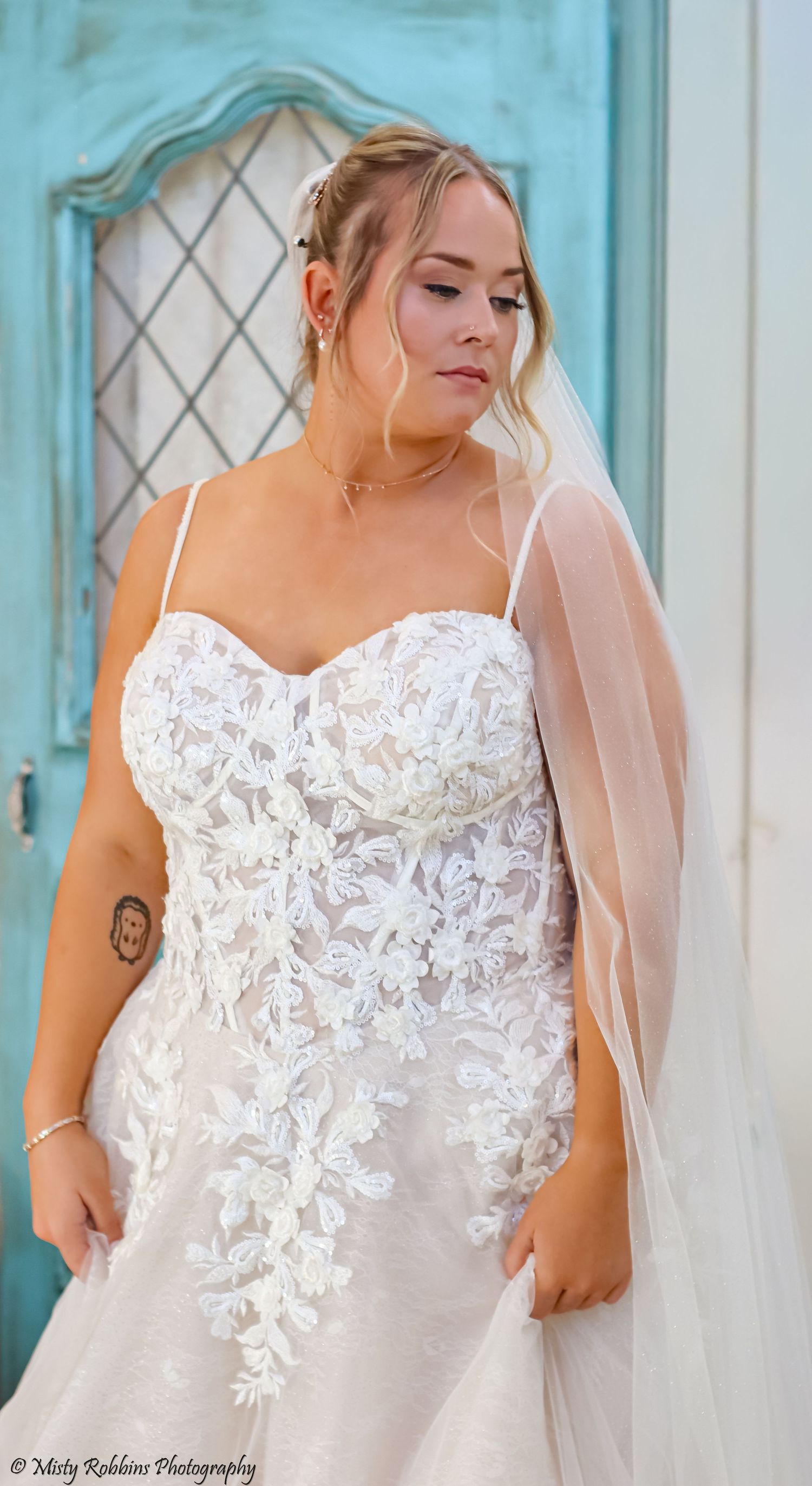 Close-up details of a white lace wedding dress bodice with delicate floral appliques against a turquoise background.