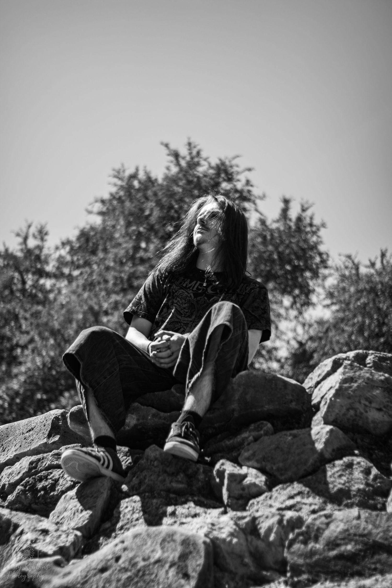 A person lies back on rocky terrain against a cloudy sky in black and white photography.