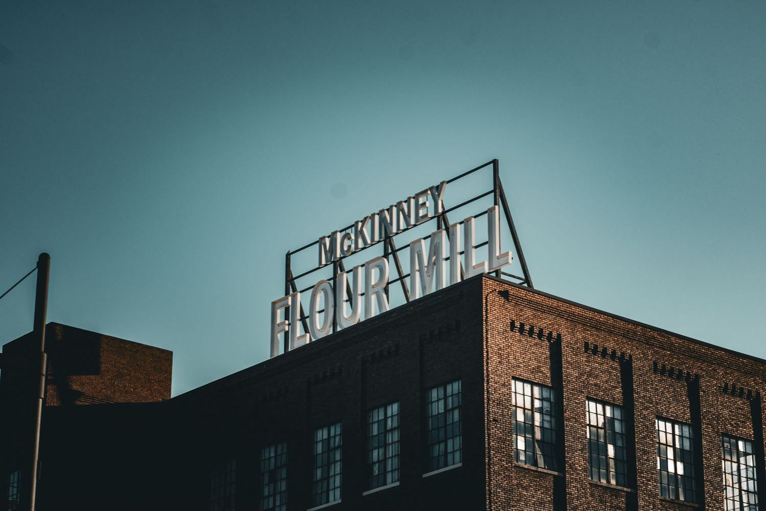 Industrial brick building with rooftop signage against a teal sky at dusk.