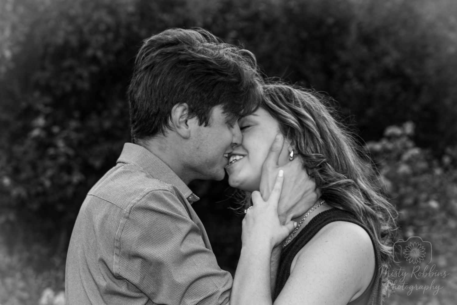 A romantic black and white portrait of a couple sharing an intimate moment outdoors in nature.