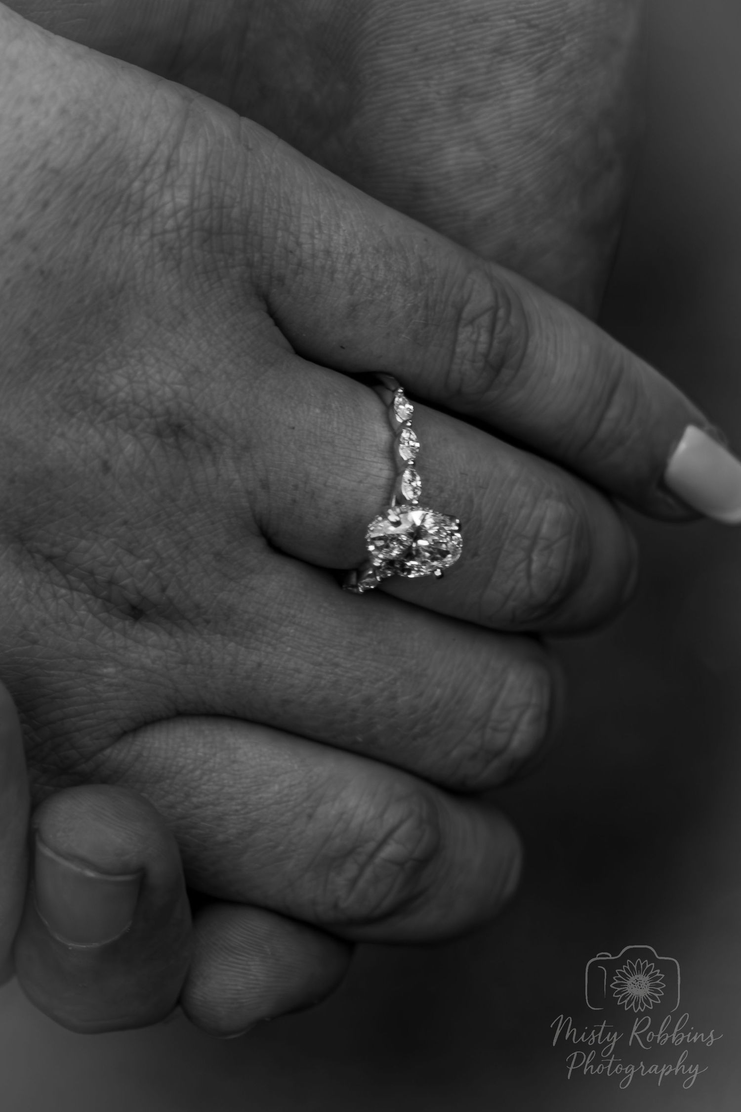 Black and white close-up of a diamond engagement ring with small accent stones on a woman's hand.