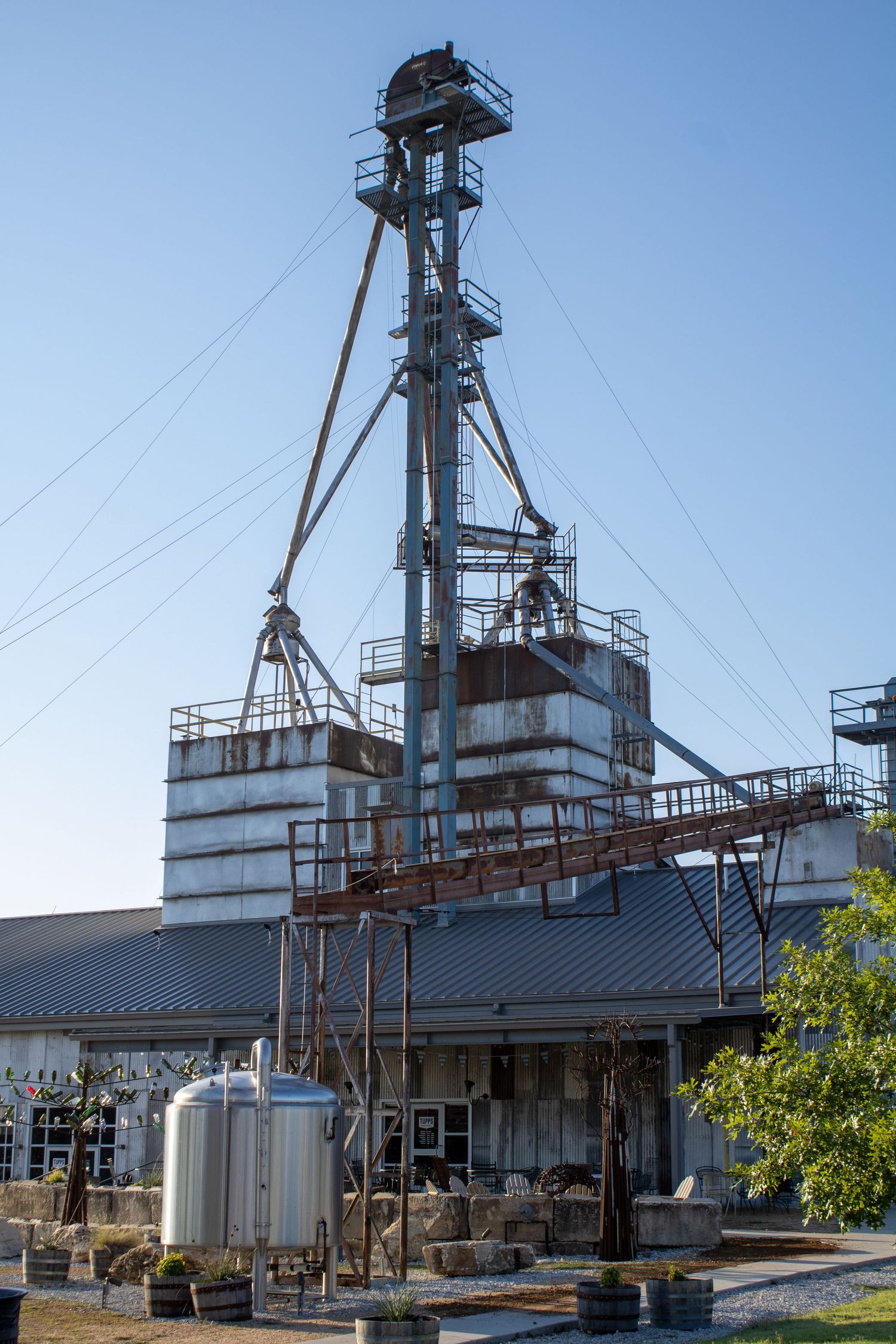 Industrial grain elevator and storage facility with metal towers against a bright blue sky.