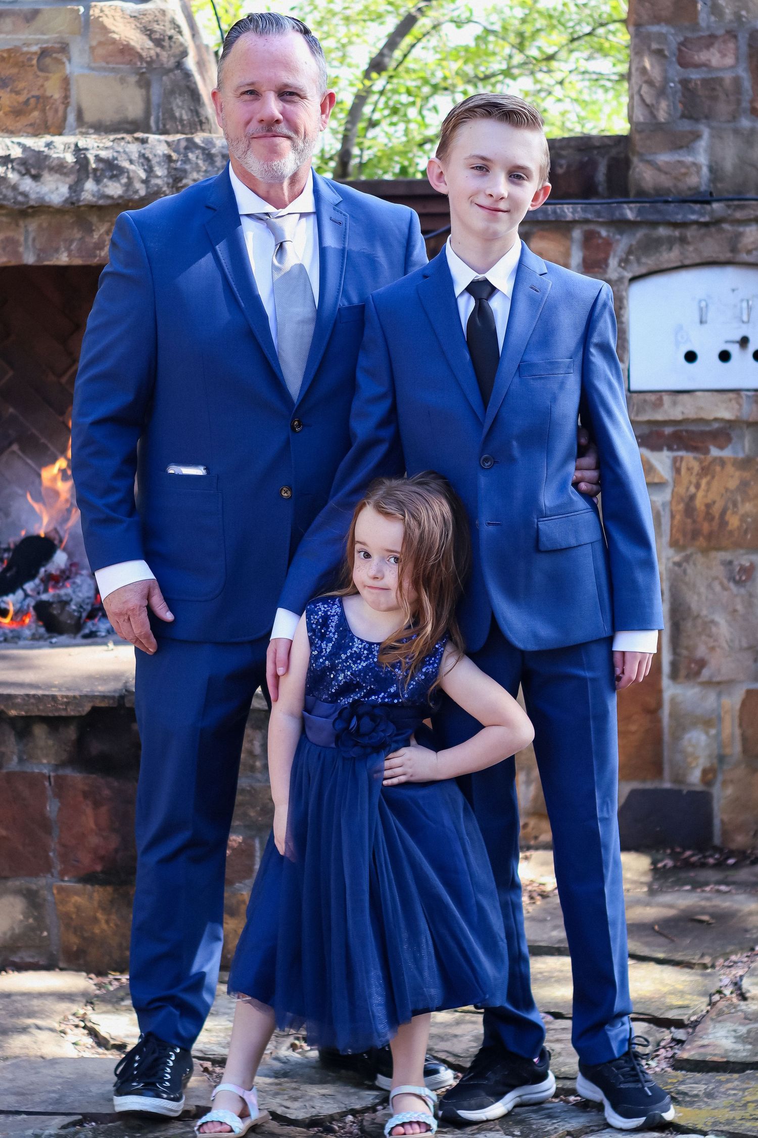 Wedding party in coordinating navy blue attire poses together against stone wall backdrop.