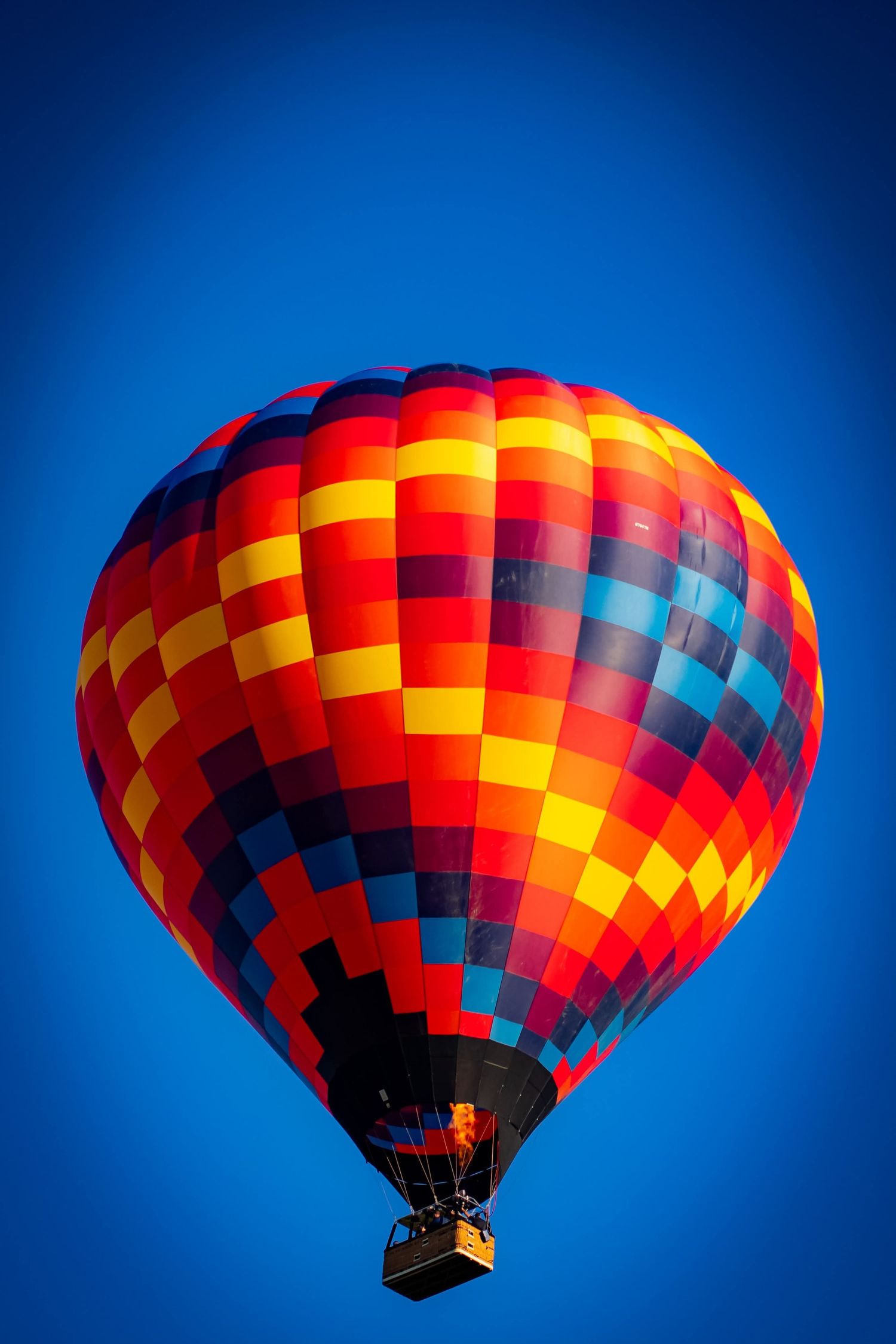 Hot air balloon with vibrant red, orange and yellow checkered pattern glowing against deep blue sky.