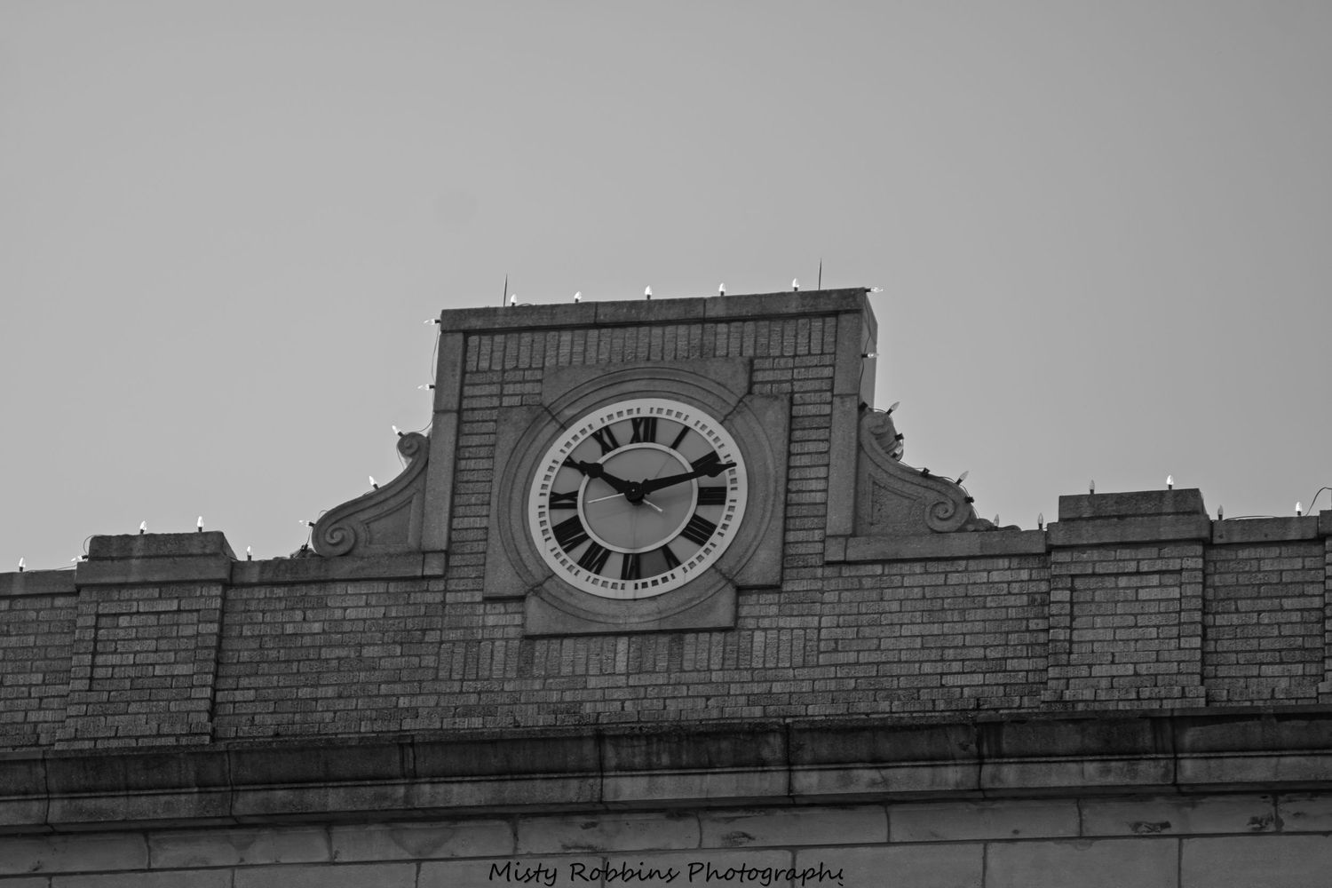 Black and white architectural detail of a vintage clock tower against a grey sky.