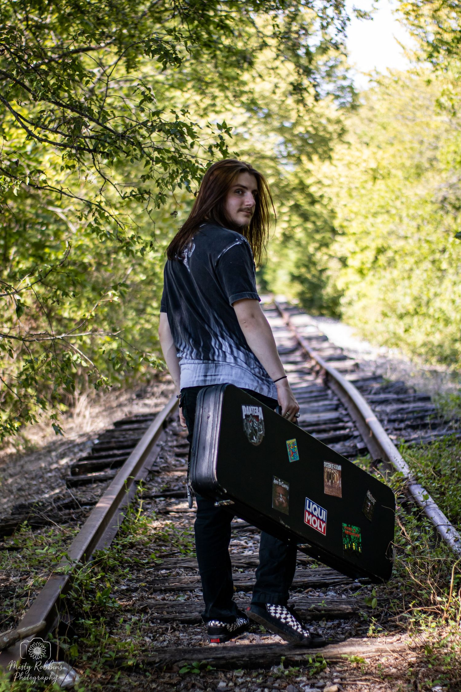 A person in dark clothing sits on abandoned train tracks surrounded by green foliage in a series of connected shots.