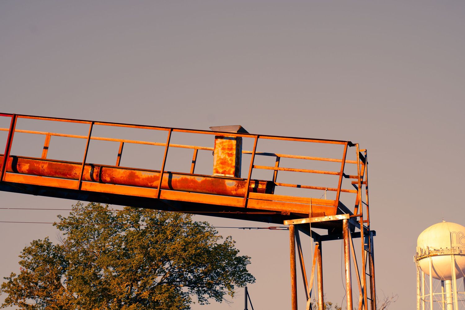 Industrial cranes and equipment silhouetted against a sunset sky with water tower in background.