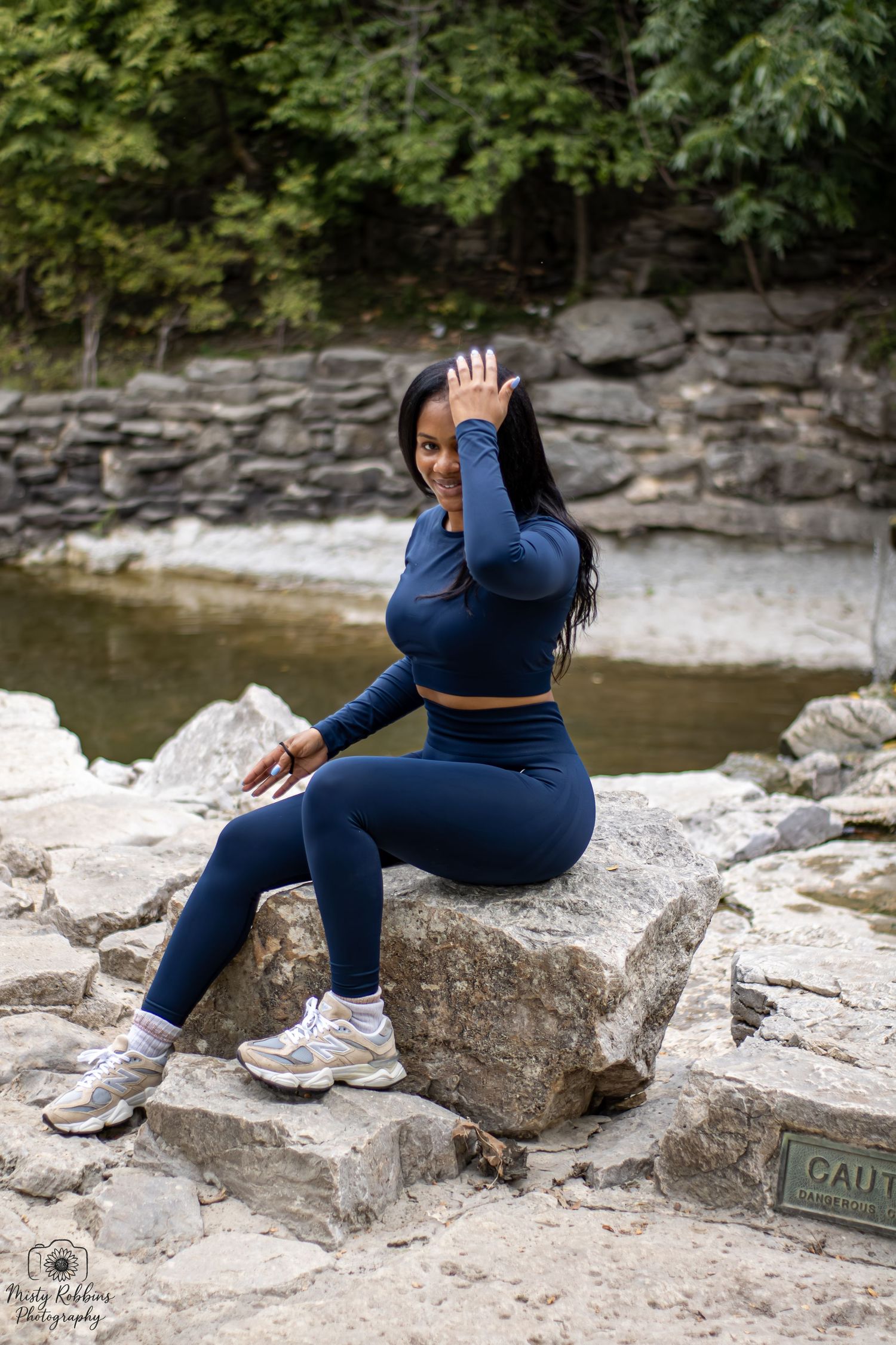 A person in blue athletic wear sits on rocky terrain near a river or stream, shown in multiple poses.