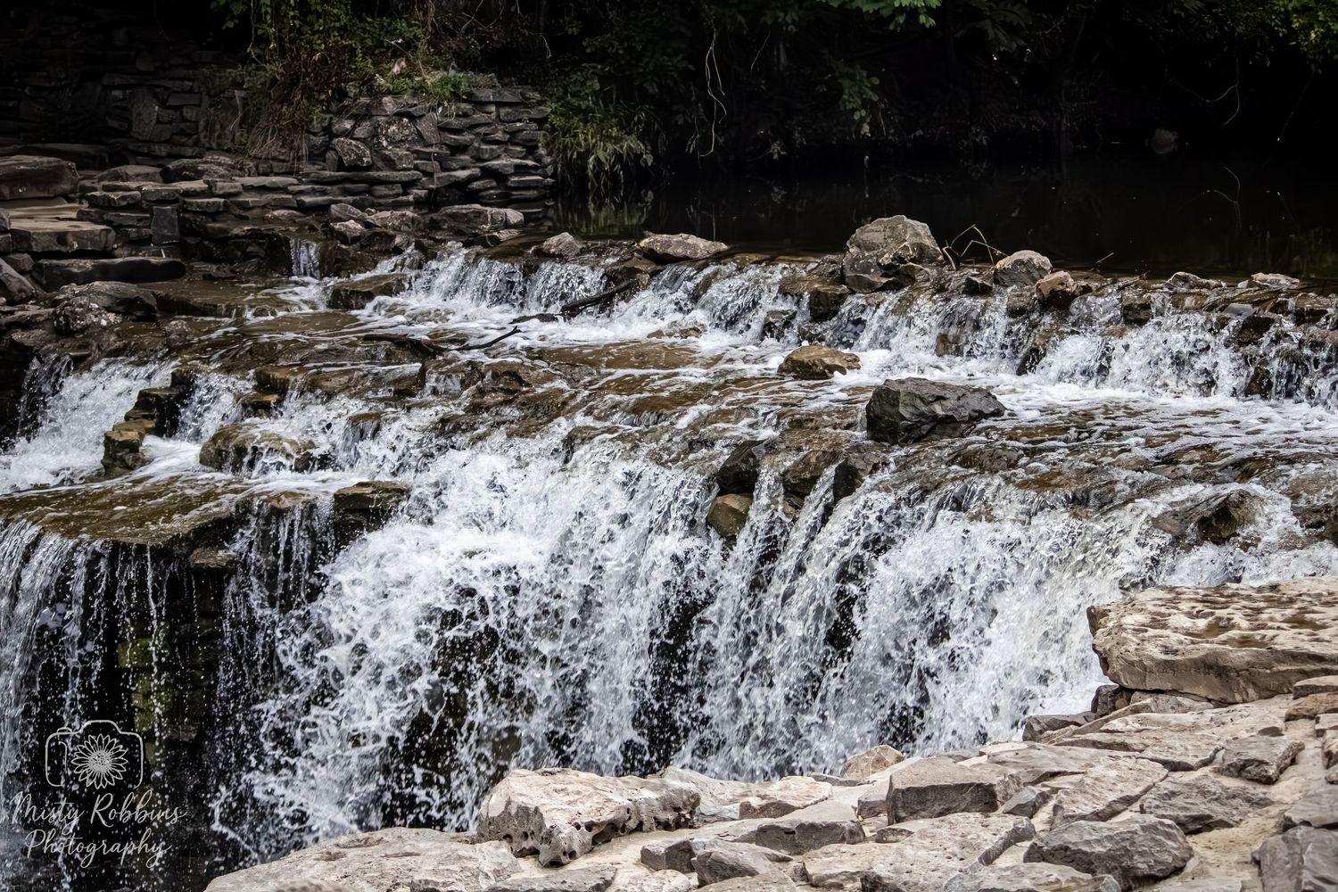Cascading waterfall flows over rocky ledges in multiple tiers creating a scenic natural landscape.