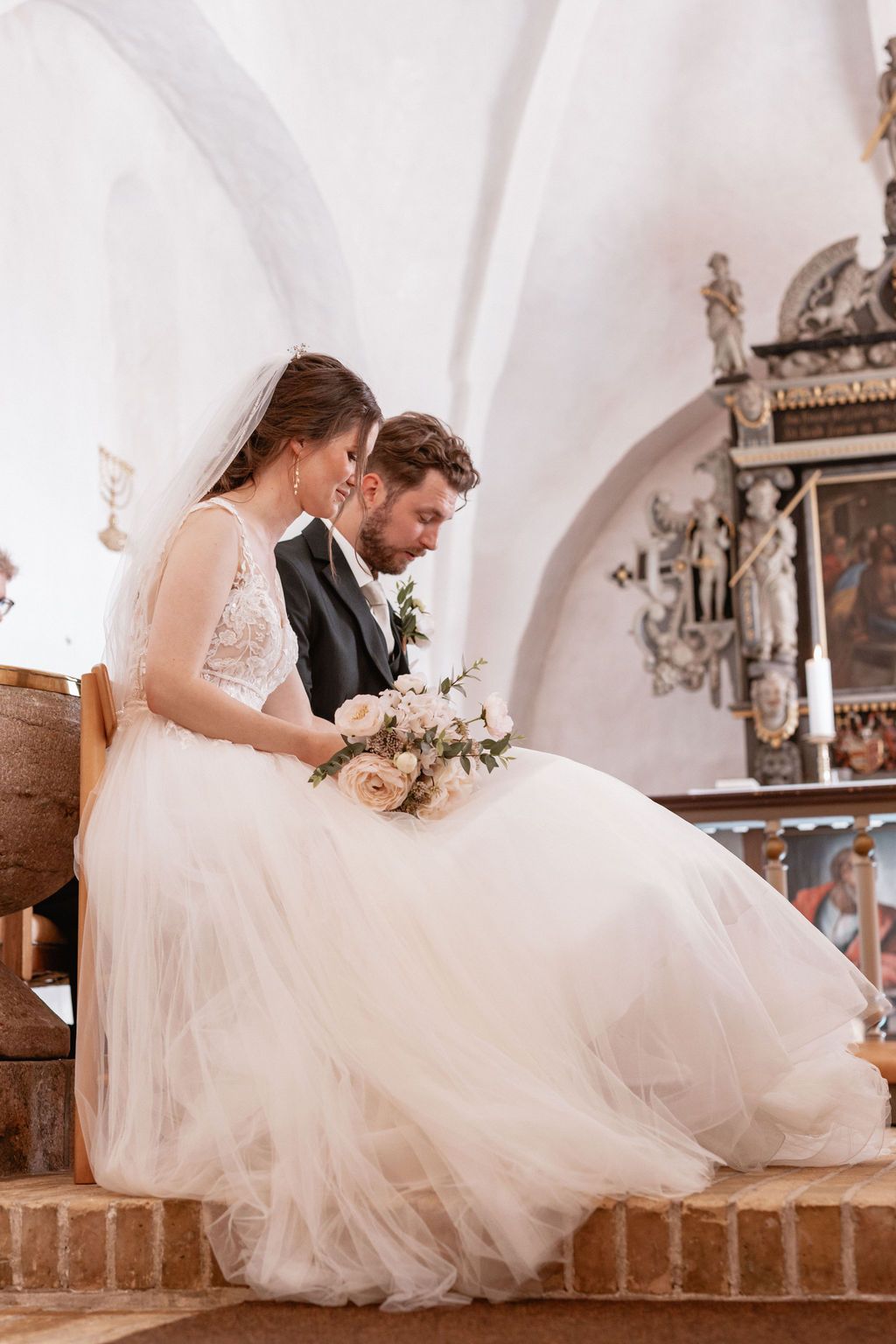 Newlyweds share intimate moments while sitting on stone steps in a historic church setting.