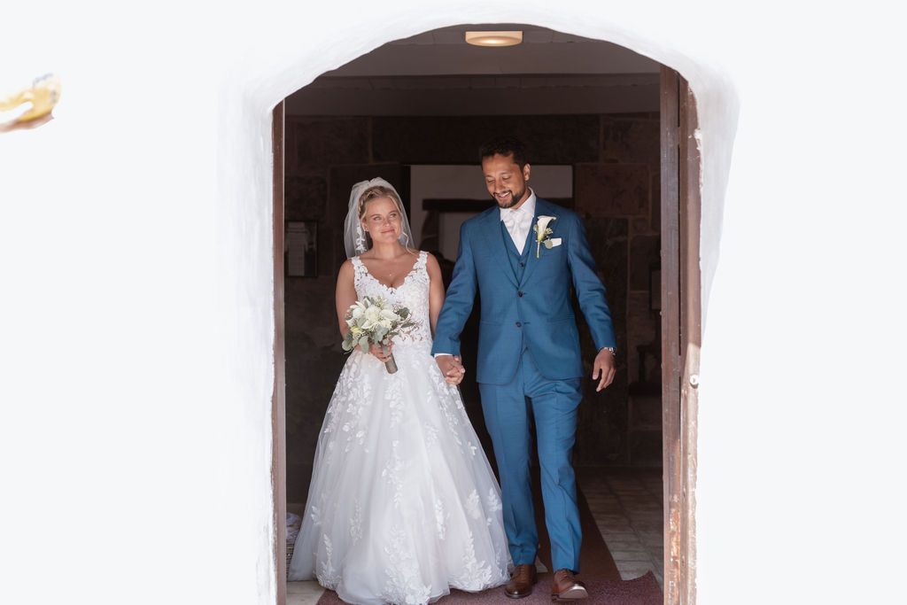 Couple emerges through stone doorway at traditional church wedding.