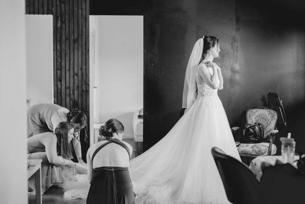 Black and white photo of wedding dress preparations with helpers adjusting the gown.